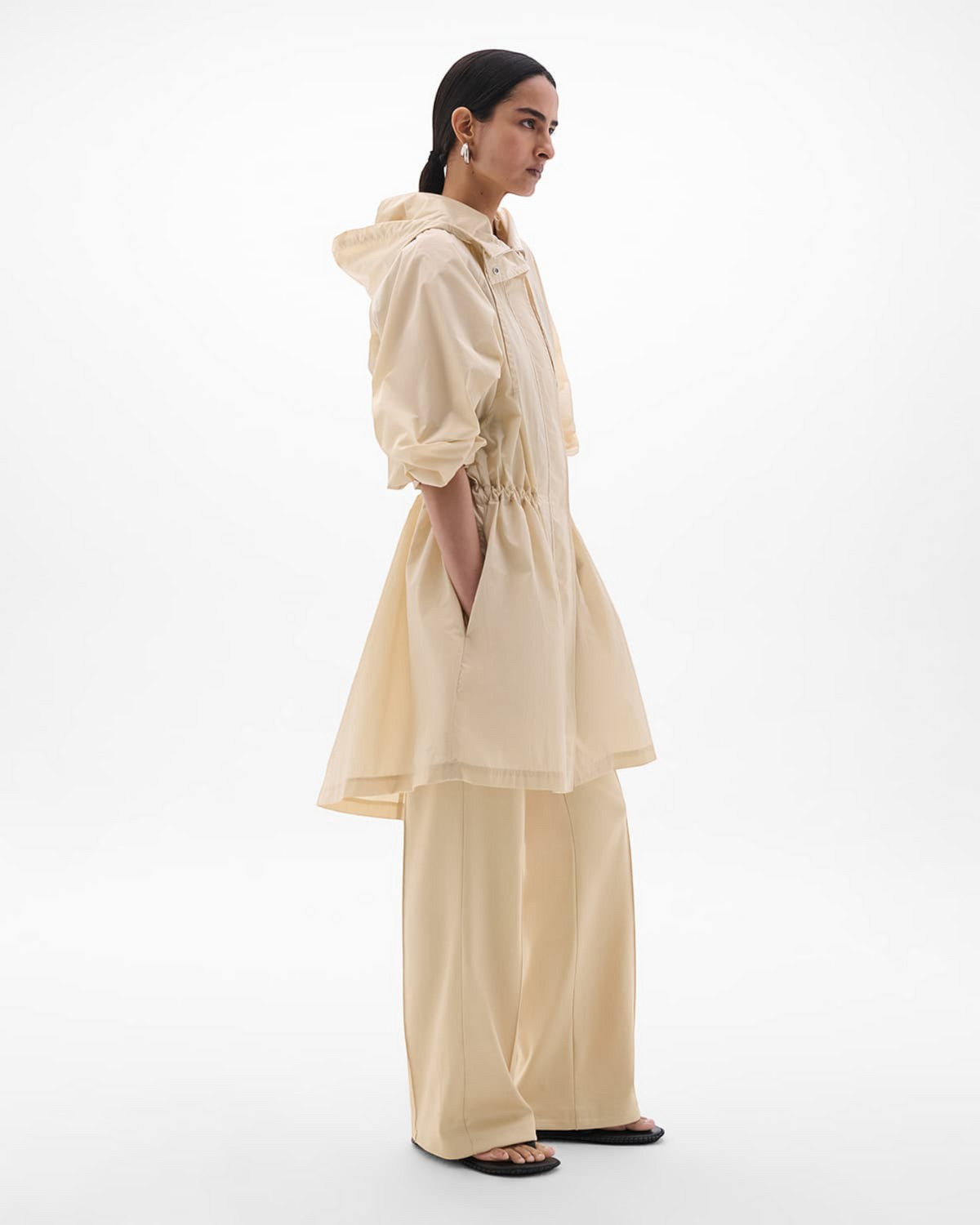 Weldun sand recycled nylon anorak with oversized hood and adjustable waist, worn by a model in profile view.