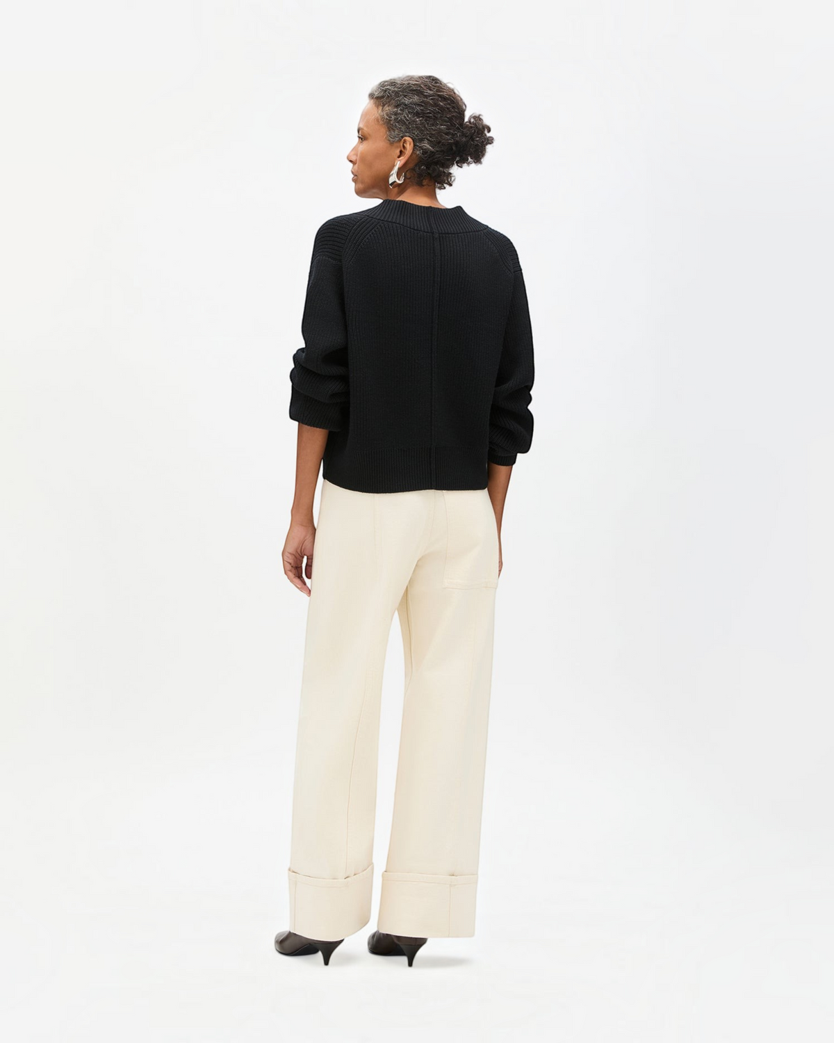 Model wearing a Weldun black ribbed cropped cardigan with dropped shoulders and back seam detail, back view.