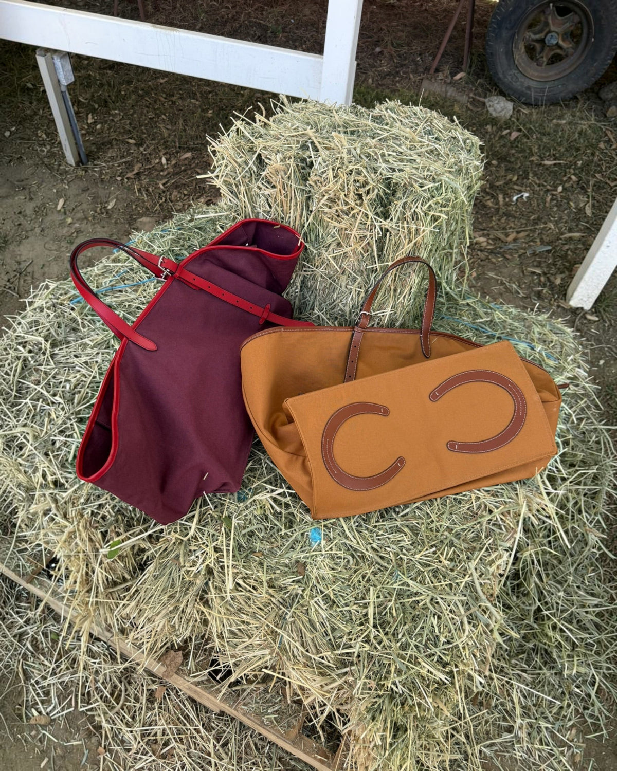 Weldun Leonora Weekend Canvas Carryall bags in burgundy and tan resting on a hay bale with leather trim details