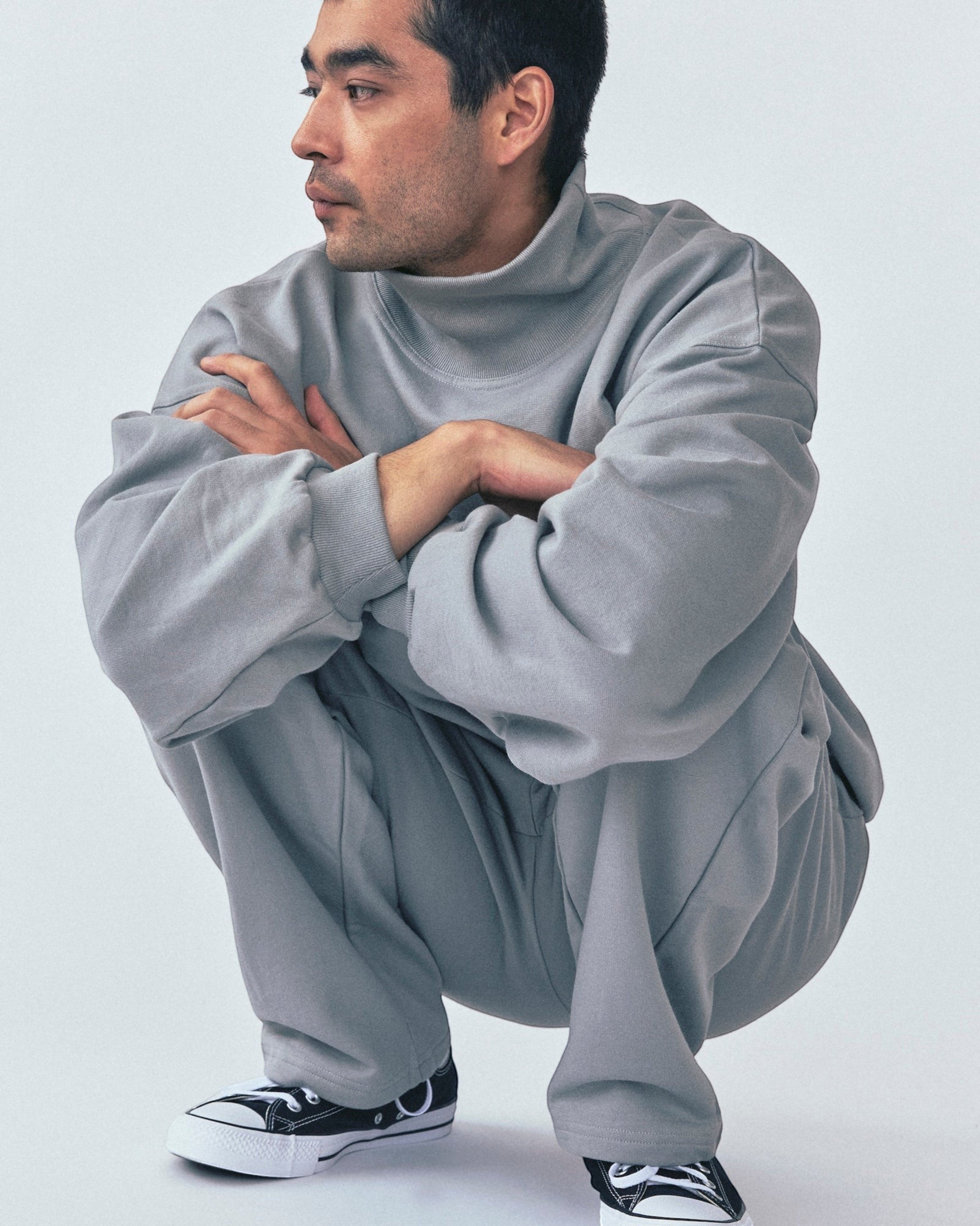 Weldun grey organic cotton high neck sweatshirt with a relaxed boxy fit worn by a man crouching in a studio setting.
