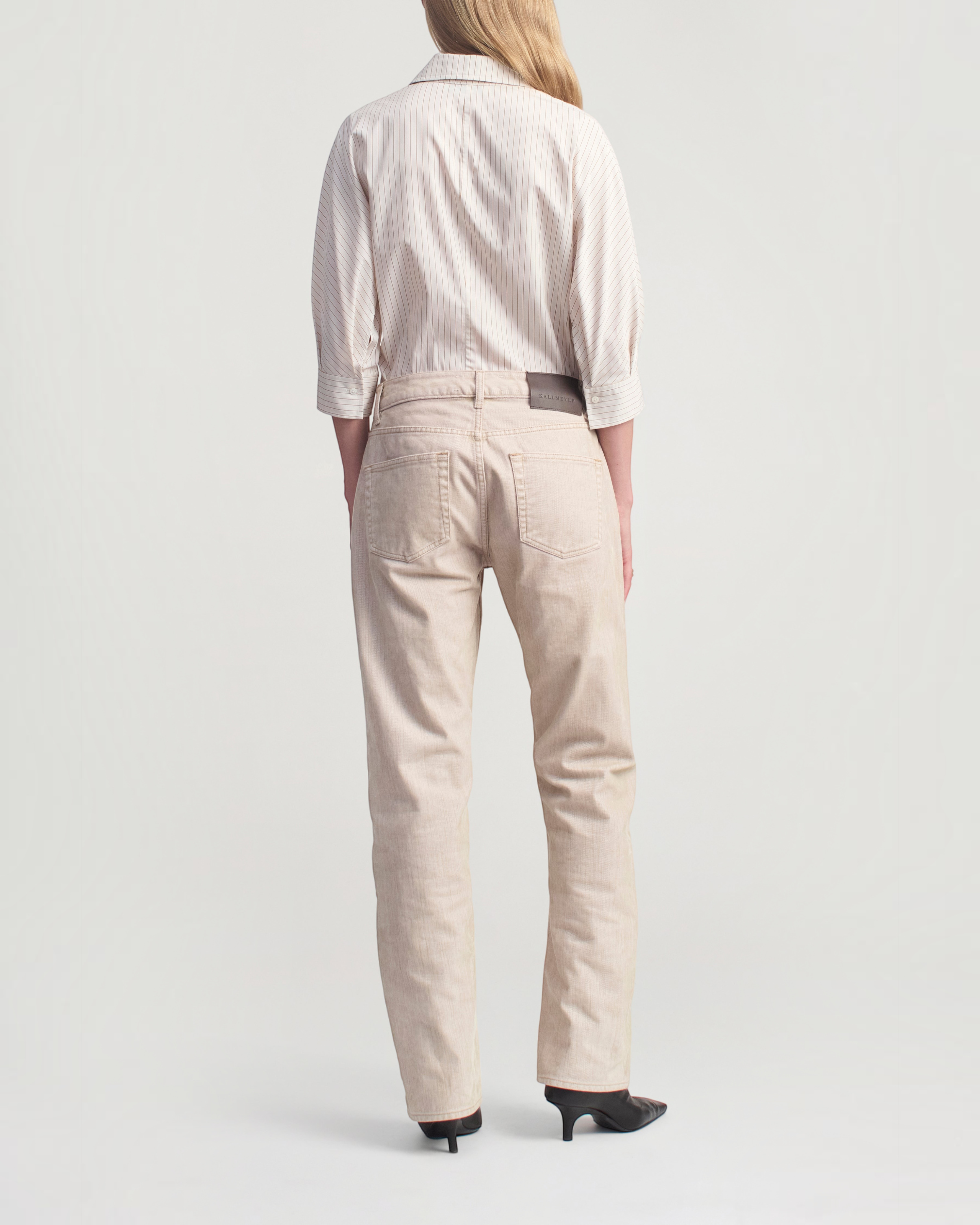 Weldun model wearing a sepia stripe cotton poplin button down shirt and light beige jeans from the back view.