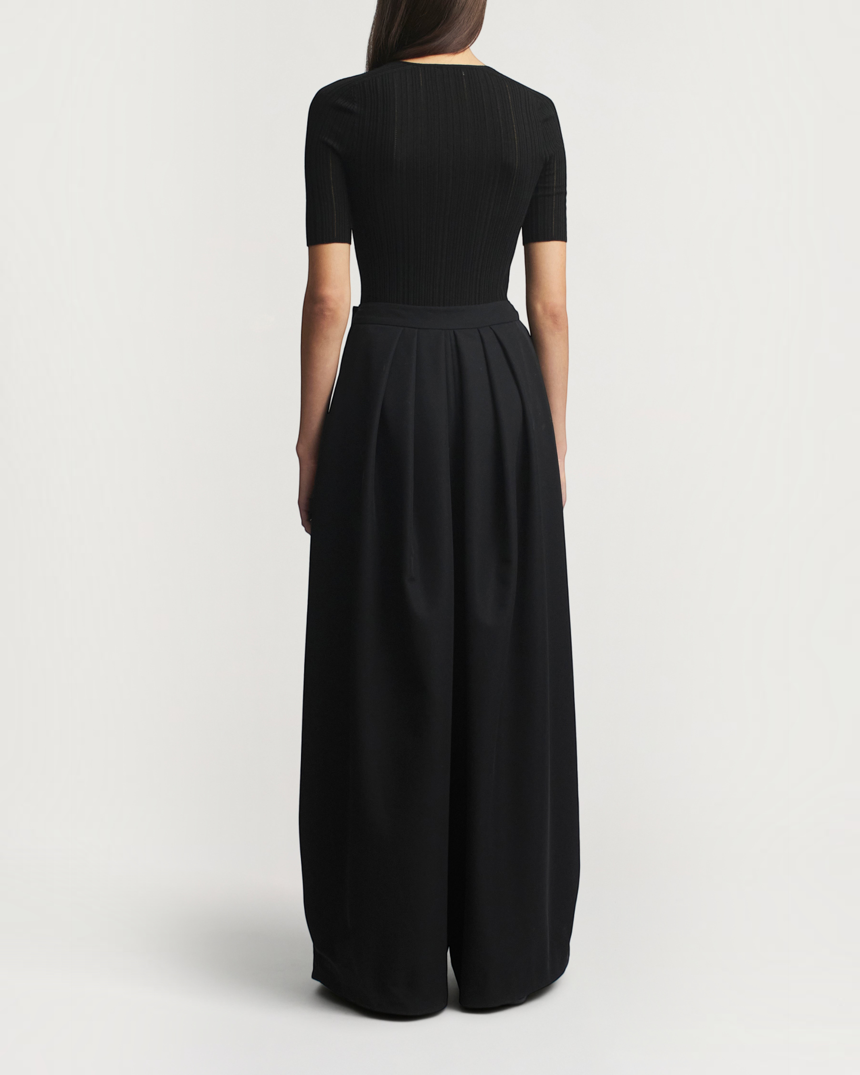 Back view of a model wearing a black Weldun Pika short sleeve V-neck top in superfine pointelle knit with wide pants