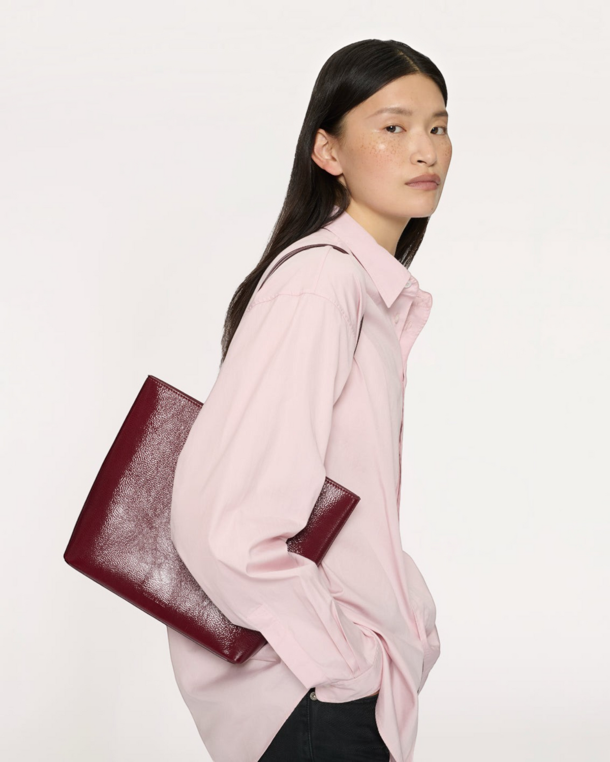 Weldun Filo Tote in claret laminated Italian leather with structured silhouette carried on shoulder by a model