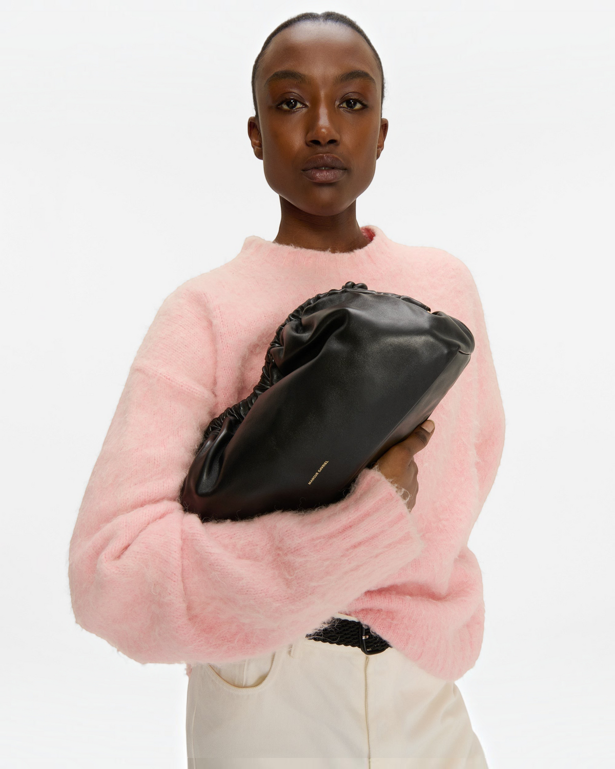 Weldun Mansur Gavriel Oversized Cloud Clutch in ebony lambskin leather held by a model in a pink sweater
