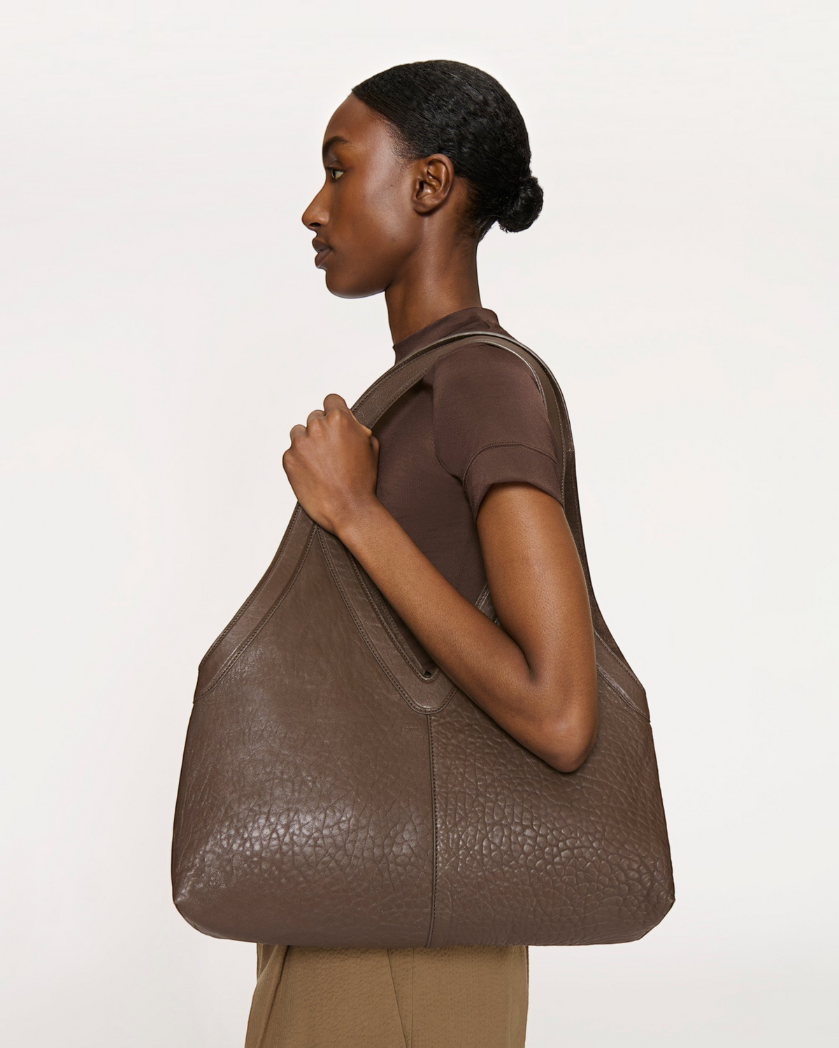 Weldun Mansur Gavriel Soft M Tote in black pebbled leather worn over the shoulder by a model in profile view