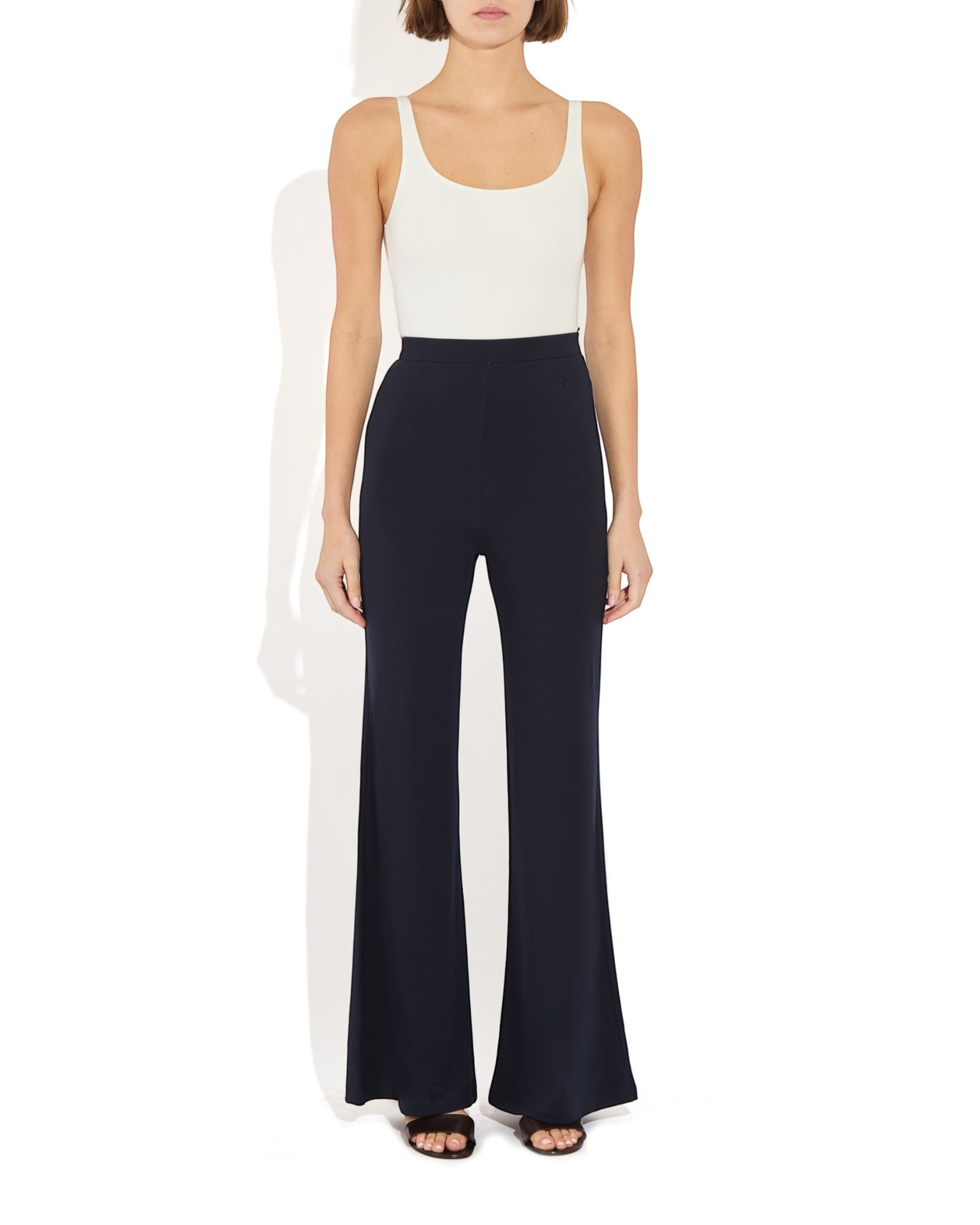 Model wearing a Weldun white scoop neck tank bodysuit tucked into high-waisted black flared trousers.