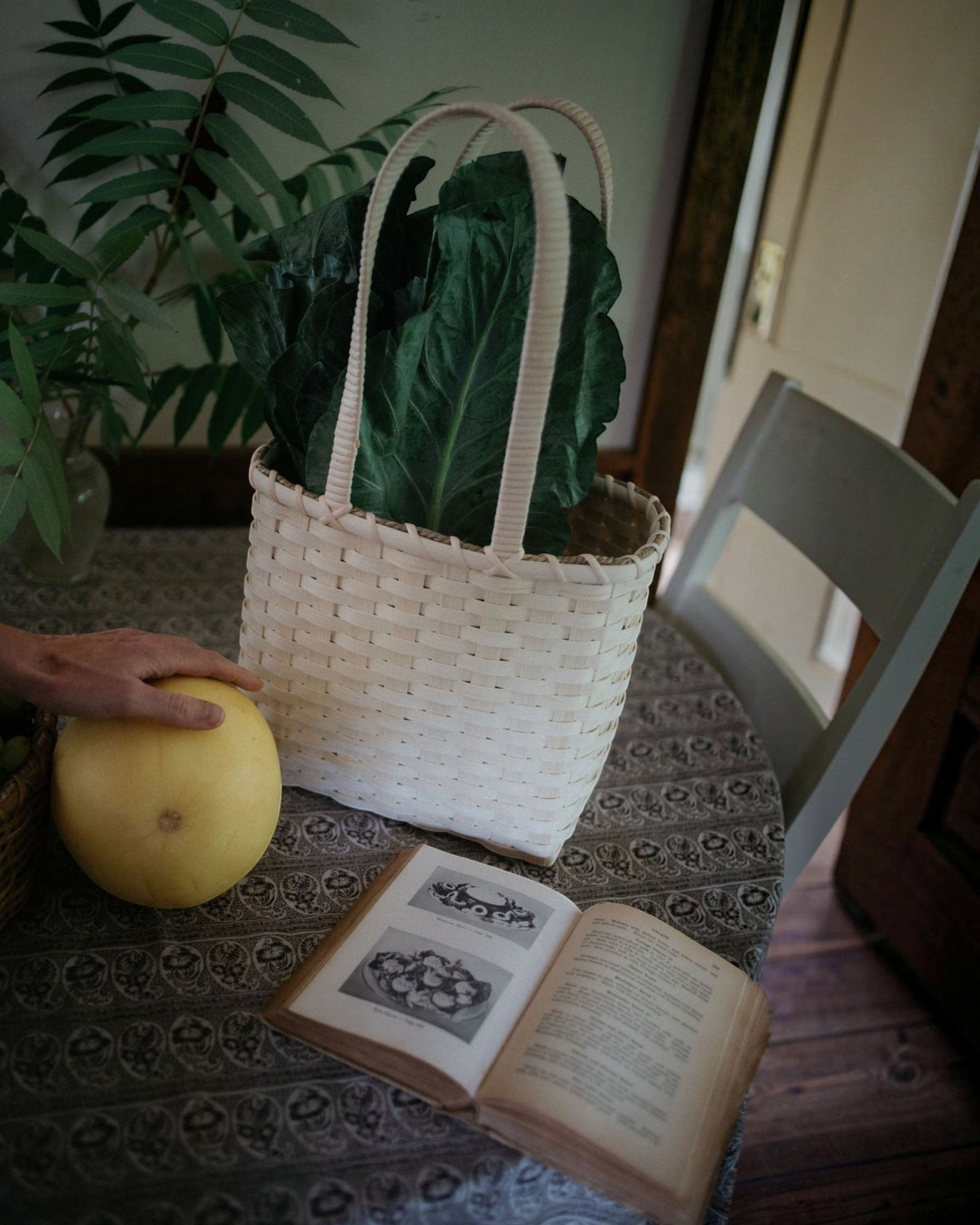 Weldun Carol lunch basket hand-woven from natural rattan with a shoulder strap, sitting on a patterned table.