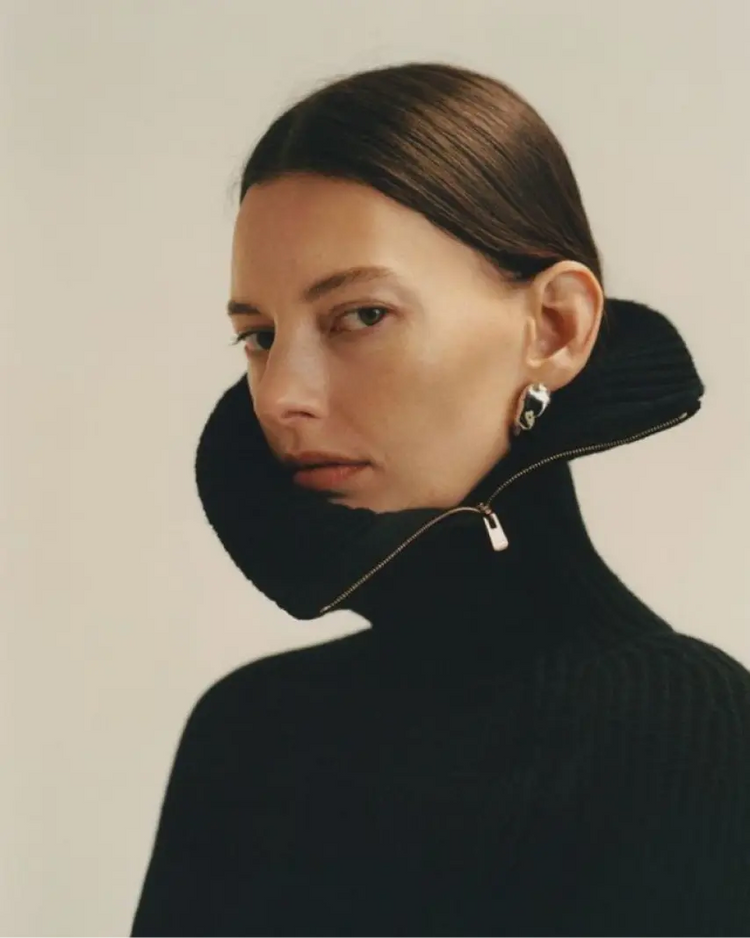 Person wearing a black turtleneck with a unique collar design on a plain background
