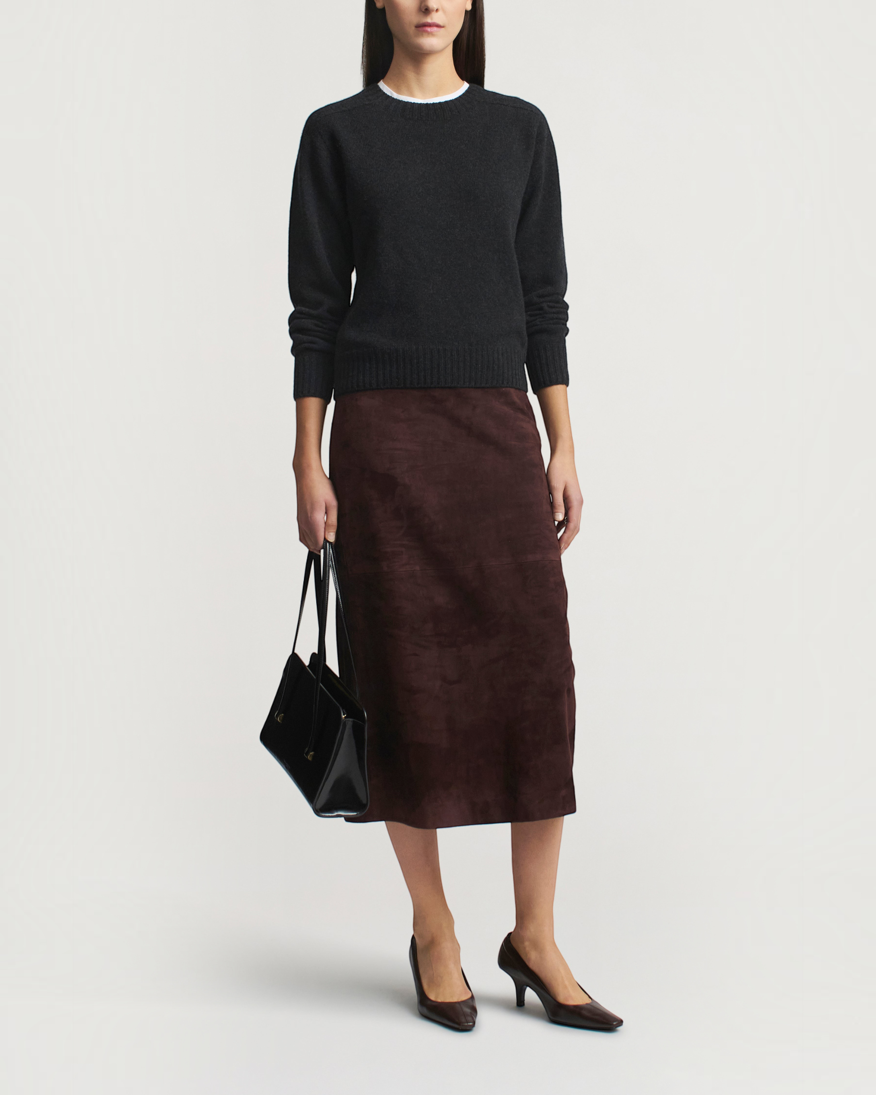 Weldun model wearing a dark grey seamless cashmere wool crewneck sweater with a brown suede midi skirt and heels.