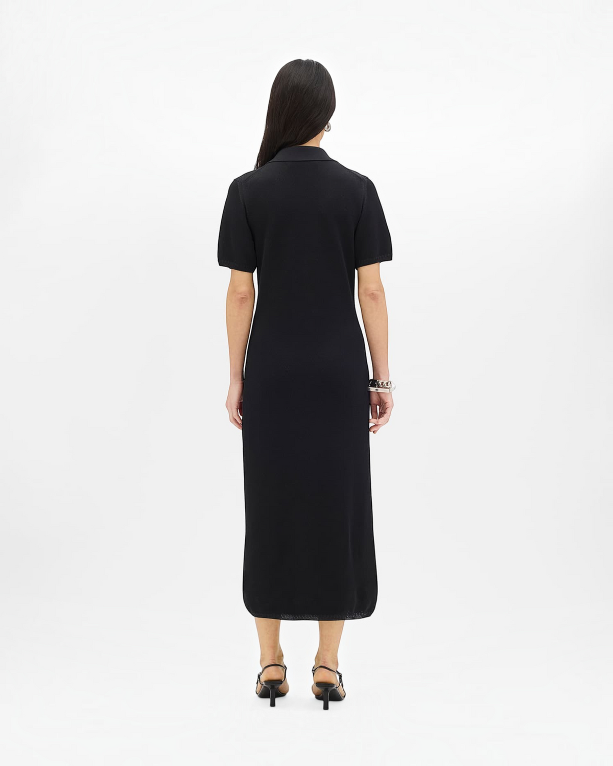 Back view of a model wearing a black Weldun midi-length pique polo dress with short sleeves and a relaxed slim fit.