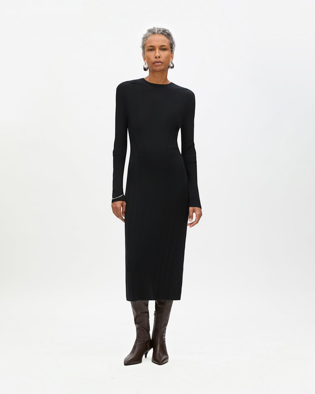 Weldun black rib knit tea length dress with long sleeves and curved seaming worn by a model with brown boots.
