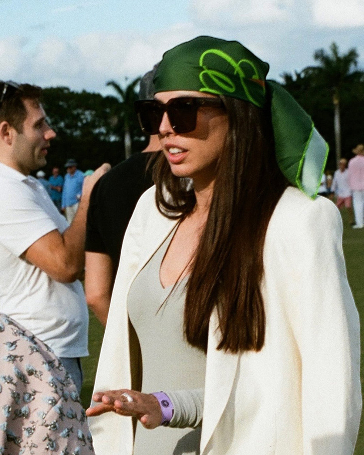 Weldun Good Girl 90 green silk twill scarf worn as a headscarf by a woman in a white blazer at an outdoor event