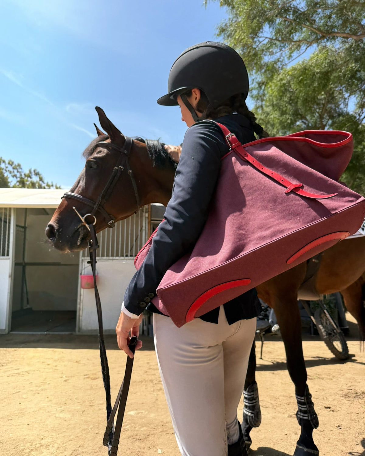 Weldun Leonora Weekend Canvas Carryall in burgundy with leather trim, worn by a rider standing next to a horse.