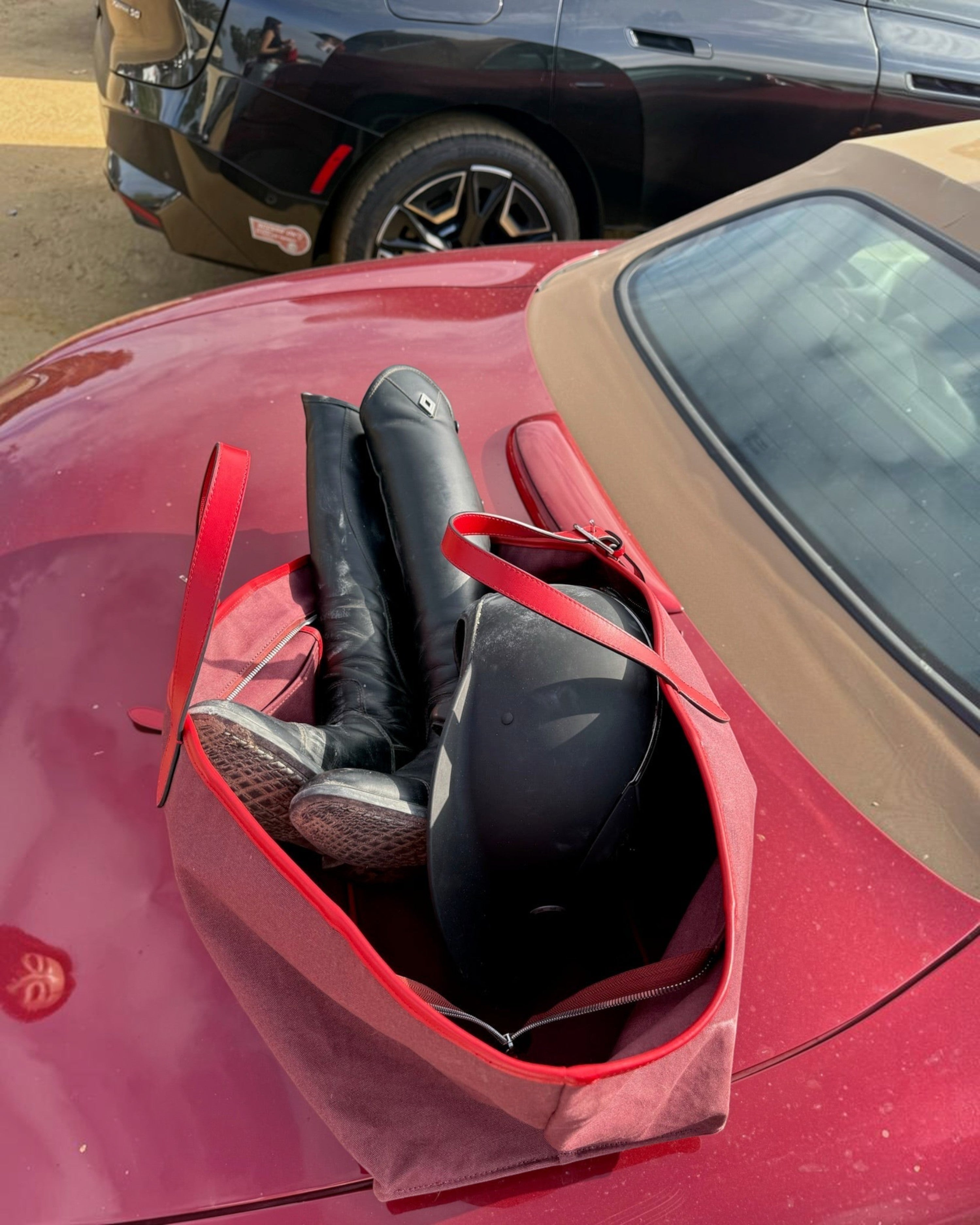 Weldun Leonora Weekend Canvas Carryall in red with leather trim, holding black riding boots and a helmet on a car