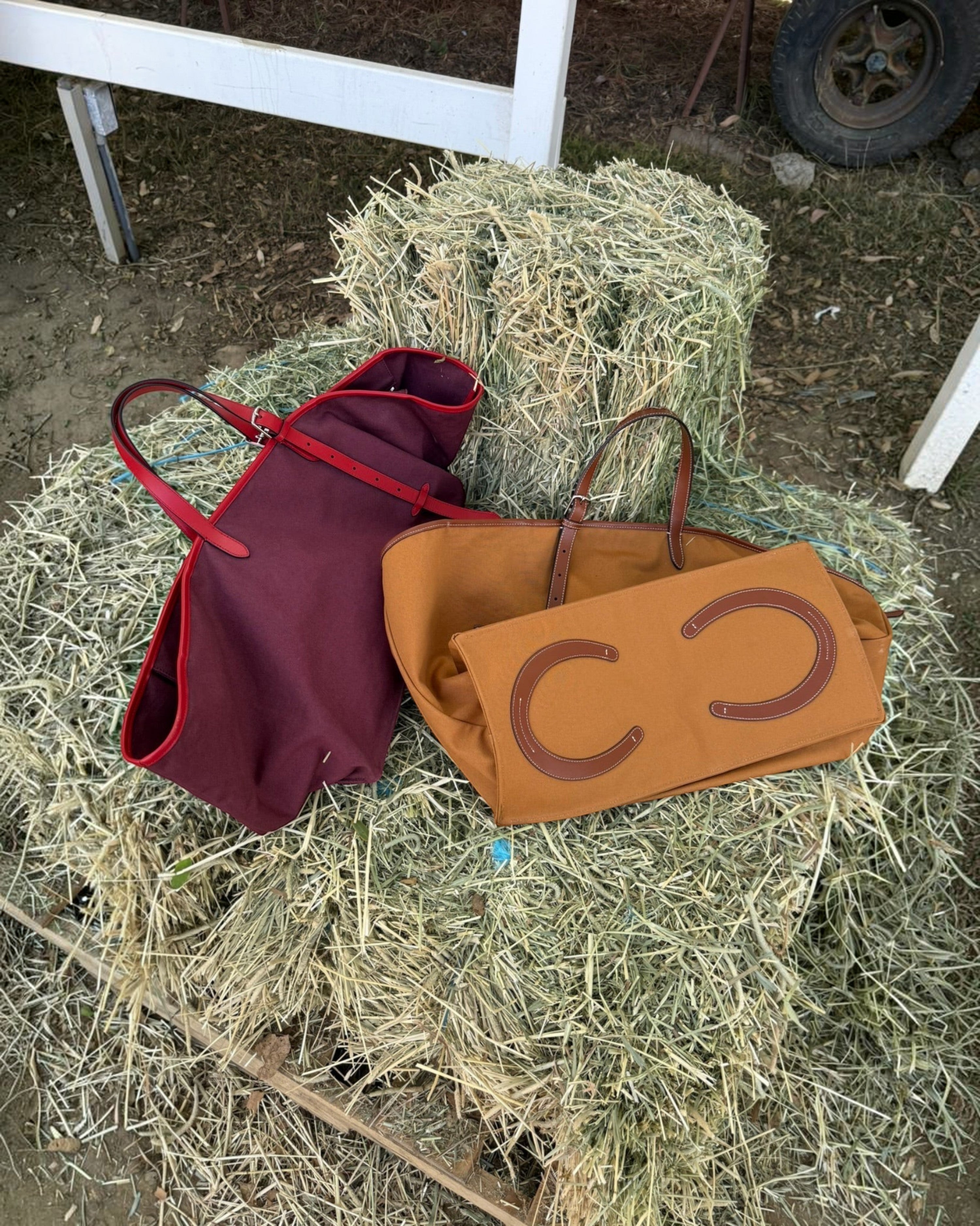 Weldun Leonora Weekend Canvas Carryall bags in burgundy and tan resting on a hay bale with leather trim details