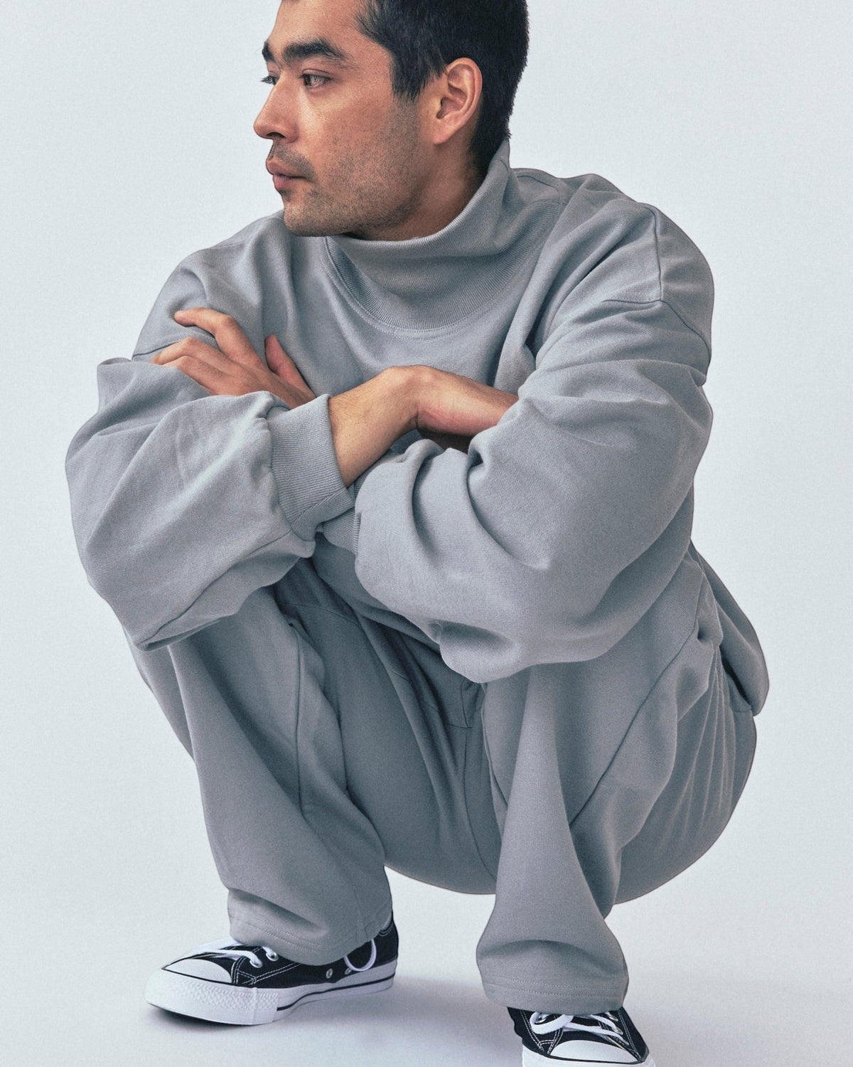 Weldun grey organic cotton high neck sweatshirt with a relaxed boxy fit worn by a man crouching in a studio setting.