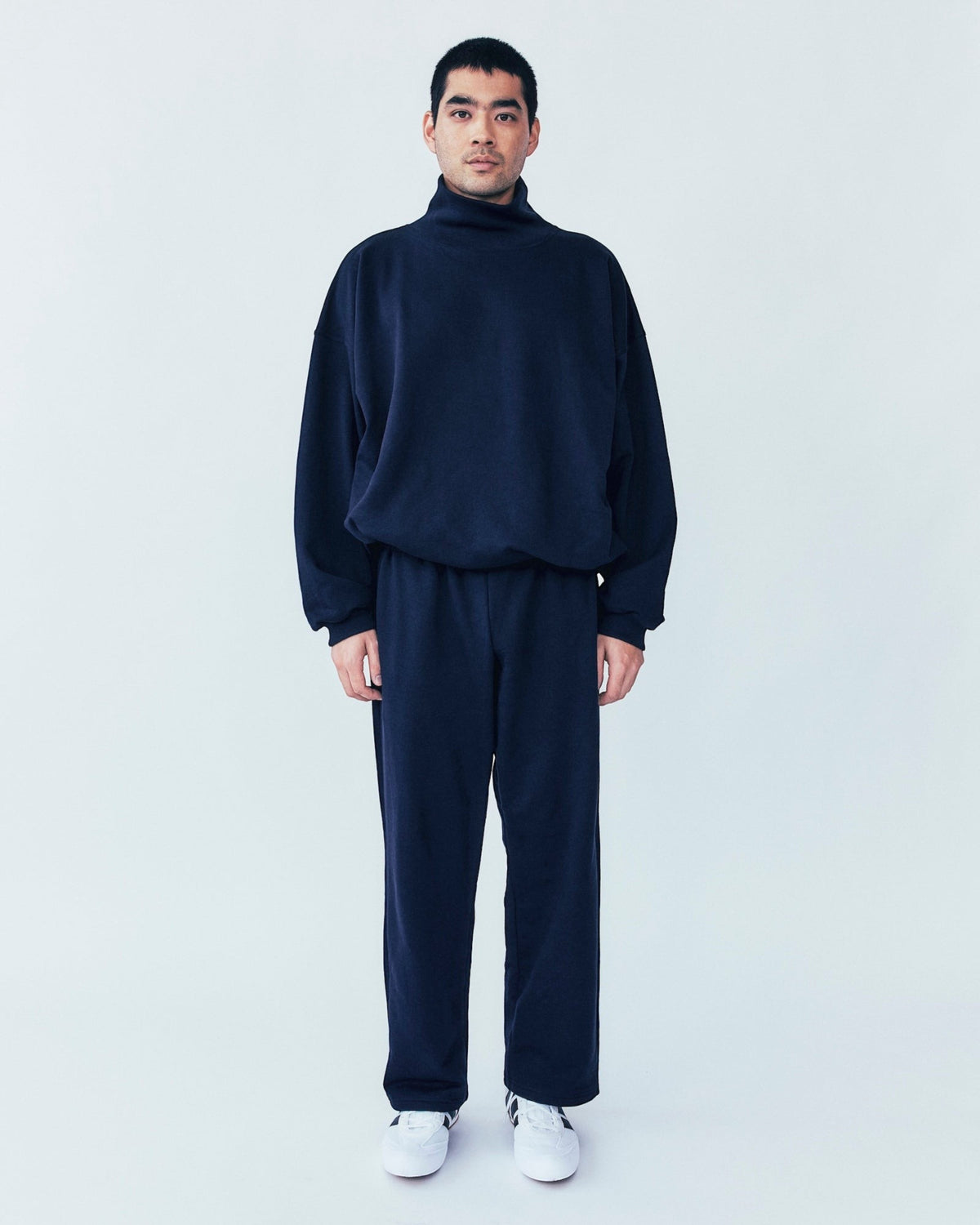 A man wearing a Weldun navy organic cotton sweatpant and matching mock neck sweatshirt with a relaxed straight fit.