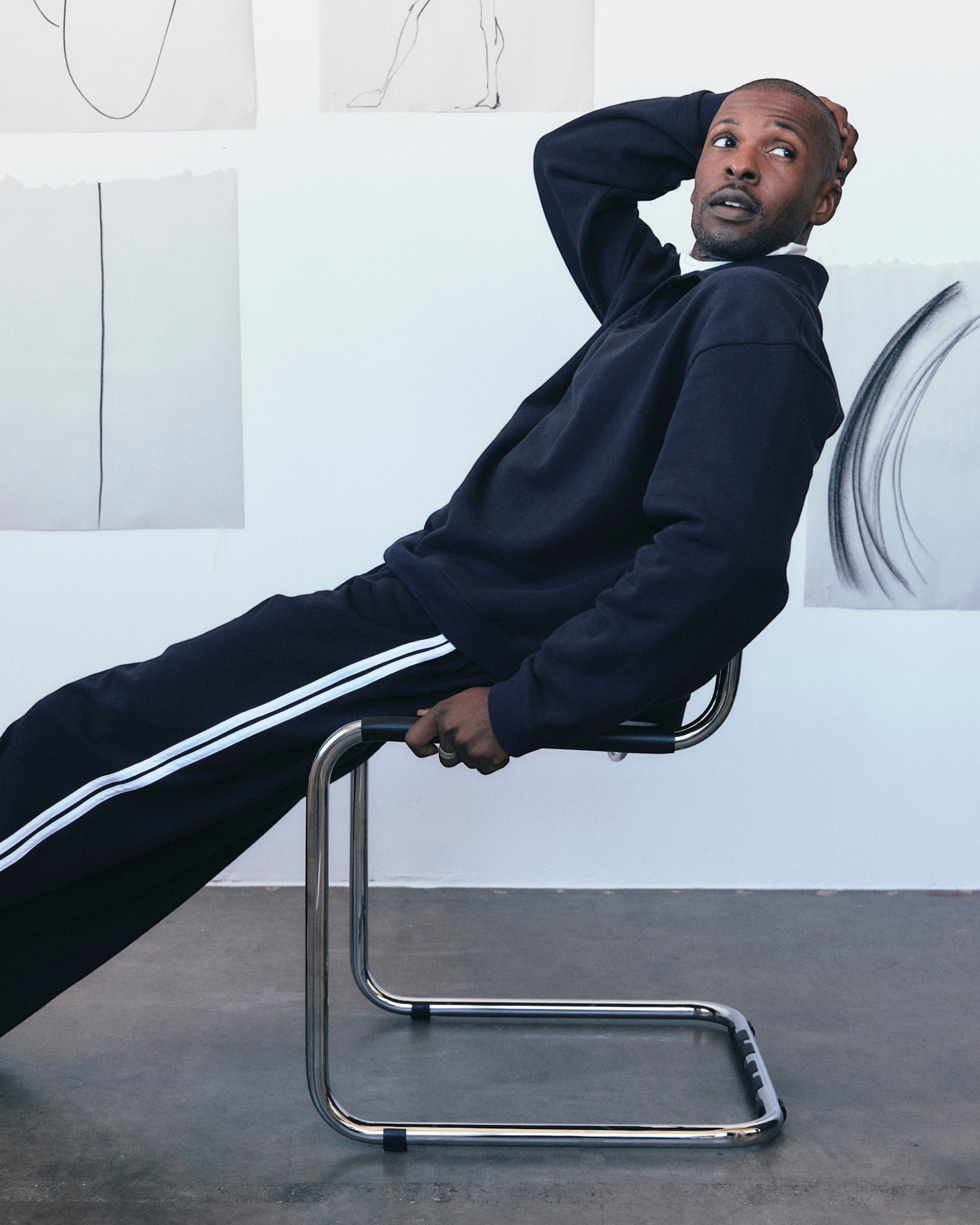 Weldun navy cotton track pants with white side stripes worn by a man sitting on a modern chair in a studio
