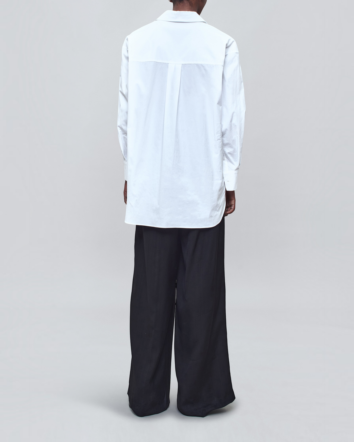 Back view of Weldun Dani white cotton poplin button down shirt with an oversized fit worn with black trousers