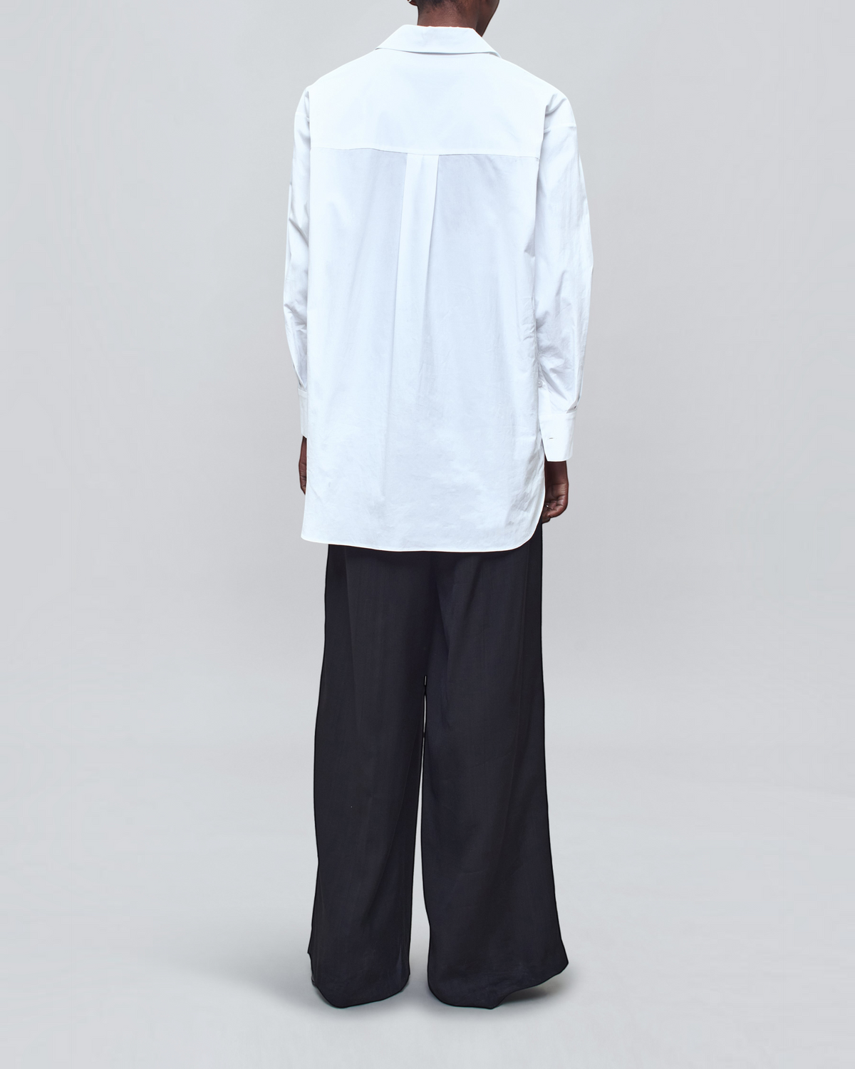 Back view of Weldun Dani white cotton poplin button down shirt with an oversized fit worn with black trousers