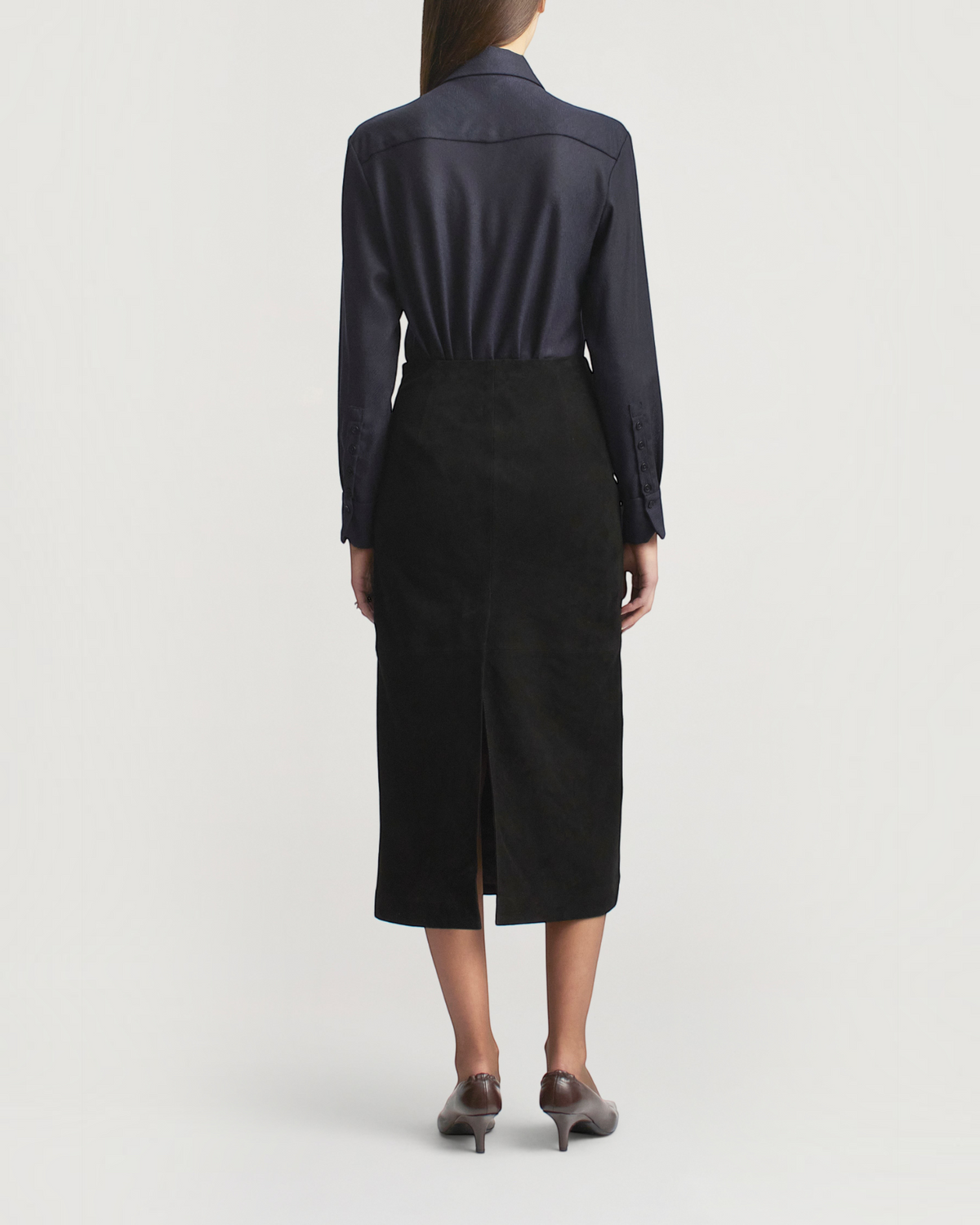 Back view of a model wearing a Weldun Joan Bias Button Down in indigo wool with a black midi skirt and heels.