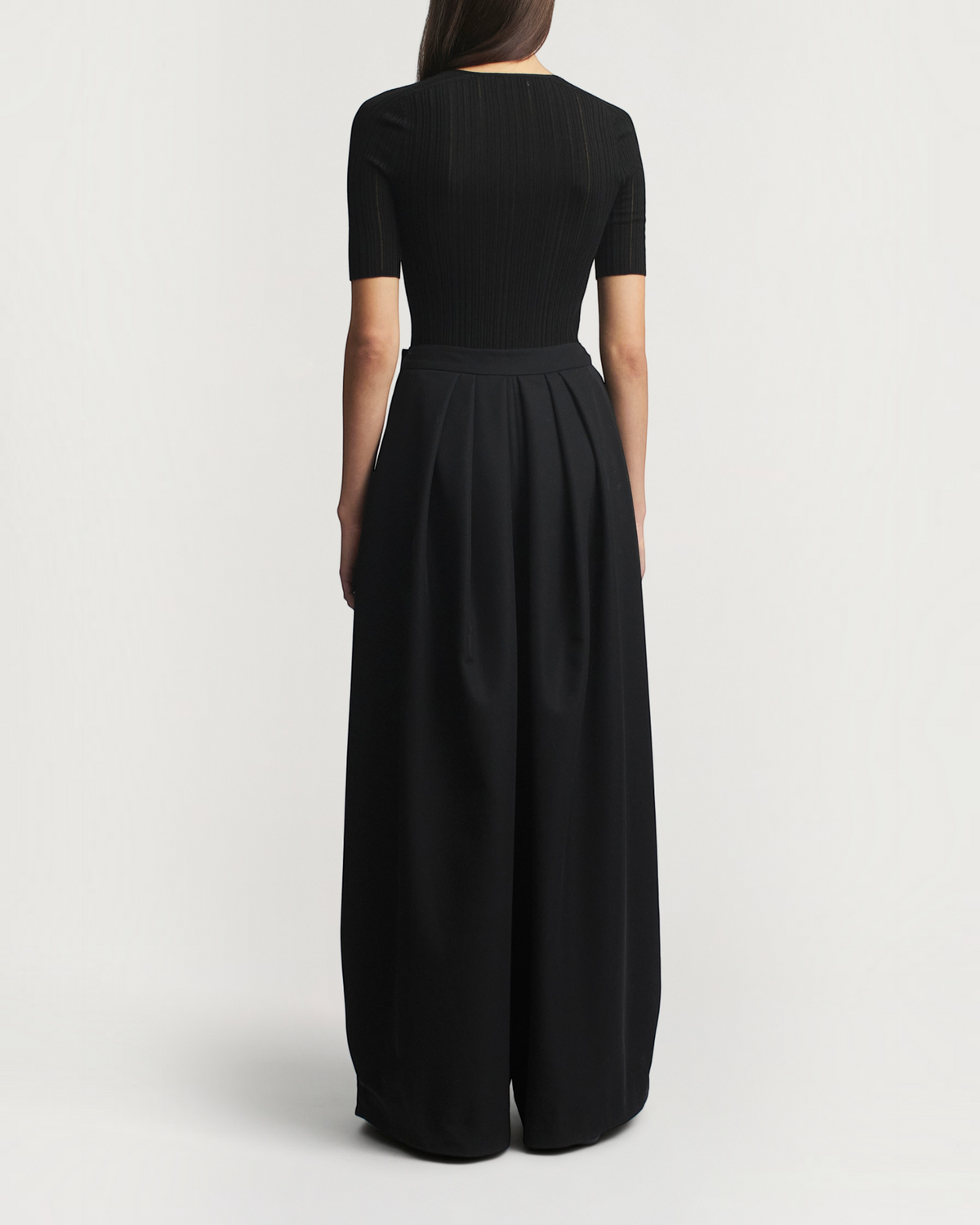 Back view of a model wearing a black Weldun Pika short sleeve V-neck top in superfine pointelle knit with wide pants