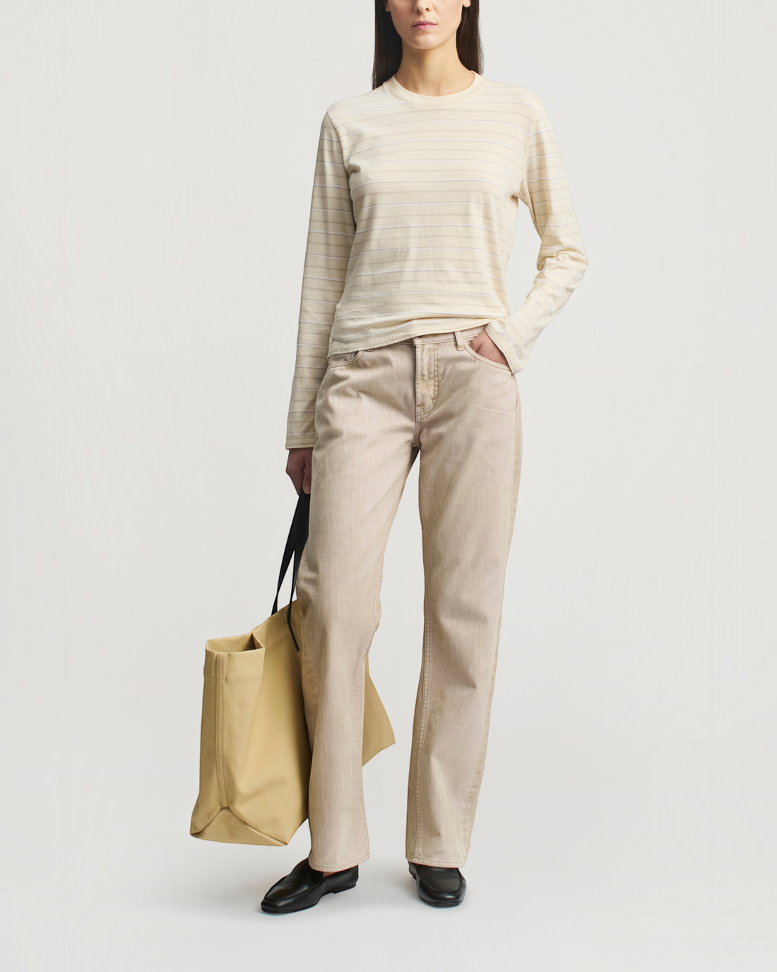 Weldun Wynn long sleeve t-shirt in ecru stripe with a relaxed boxy fit, paired with beige trousers and a tote bag.