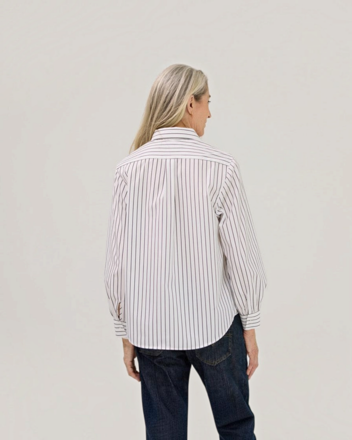 Weldun women's black and white striped long sleeve blouse with a curved hem, viewed from the back on a model.