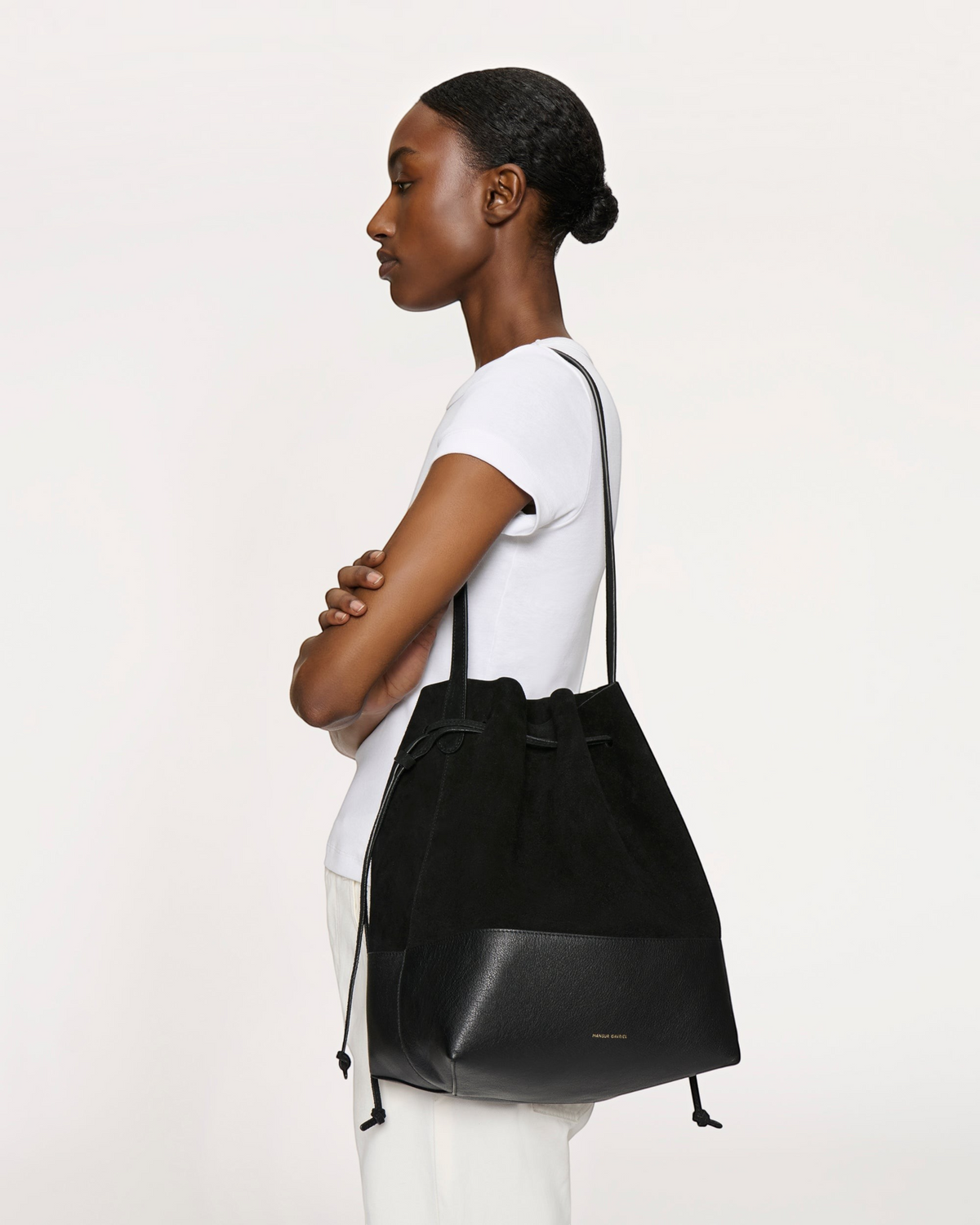 Weldun Mansur Gavriel black suede and leather drawstring bucket bag worn over the shoulder by a model