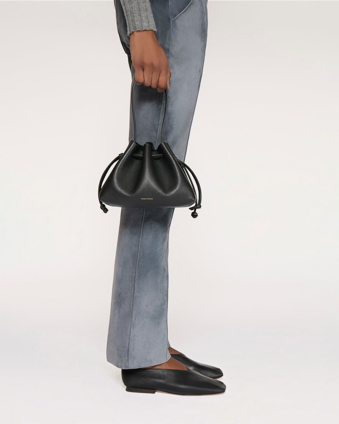 Weldun Mansur Gavriel black Italian leather drawstring pouchette held by a model wearing grey trousers.