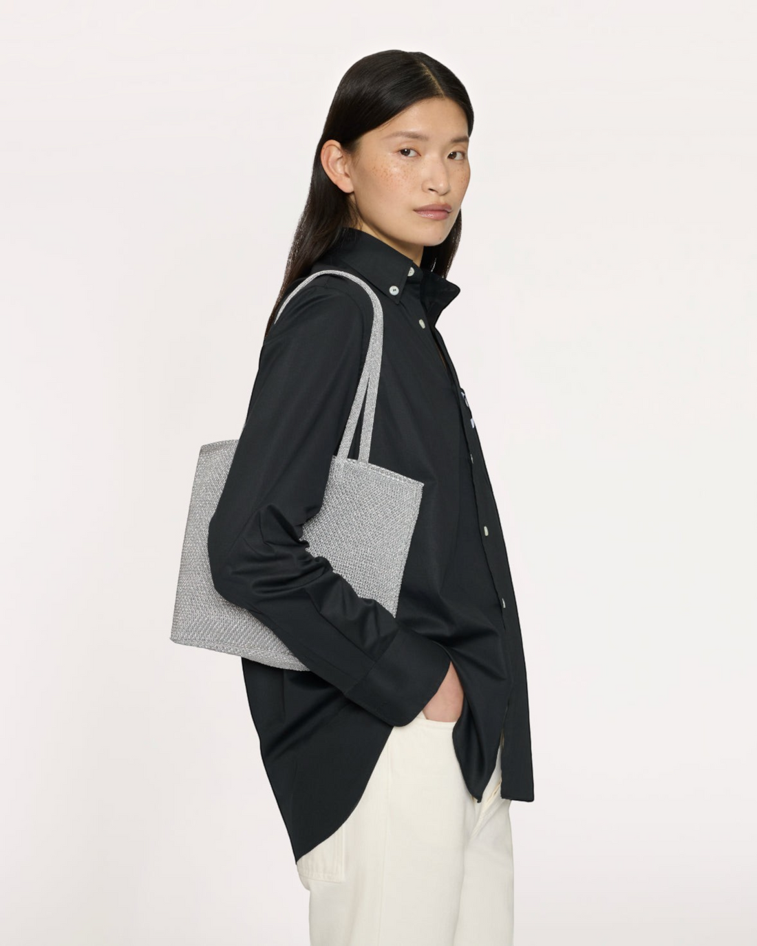 Weldun Mansur Gavriel silver metallic knit Filo tote bag worn on the shoulder by a model in a black shirt