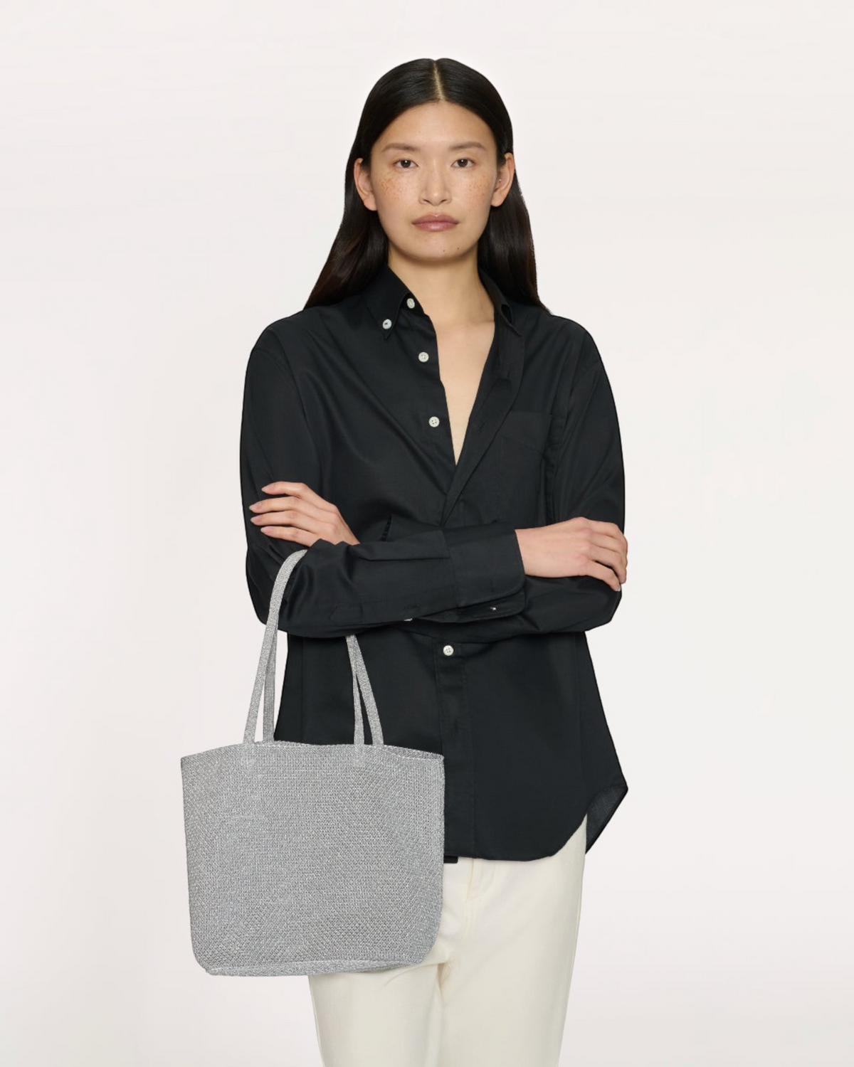 Weldun Mansur Gavriel Knit Filo Tote in shimmering silver metallic knit held by a model in a black button-down shirt.