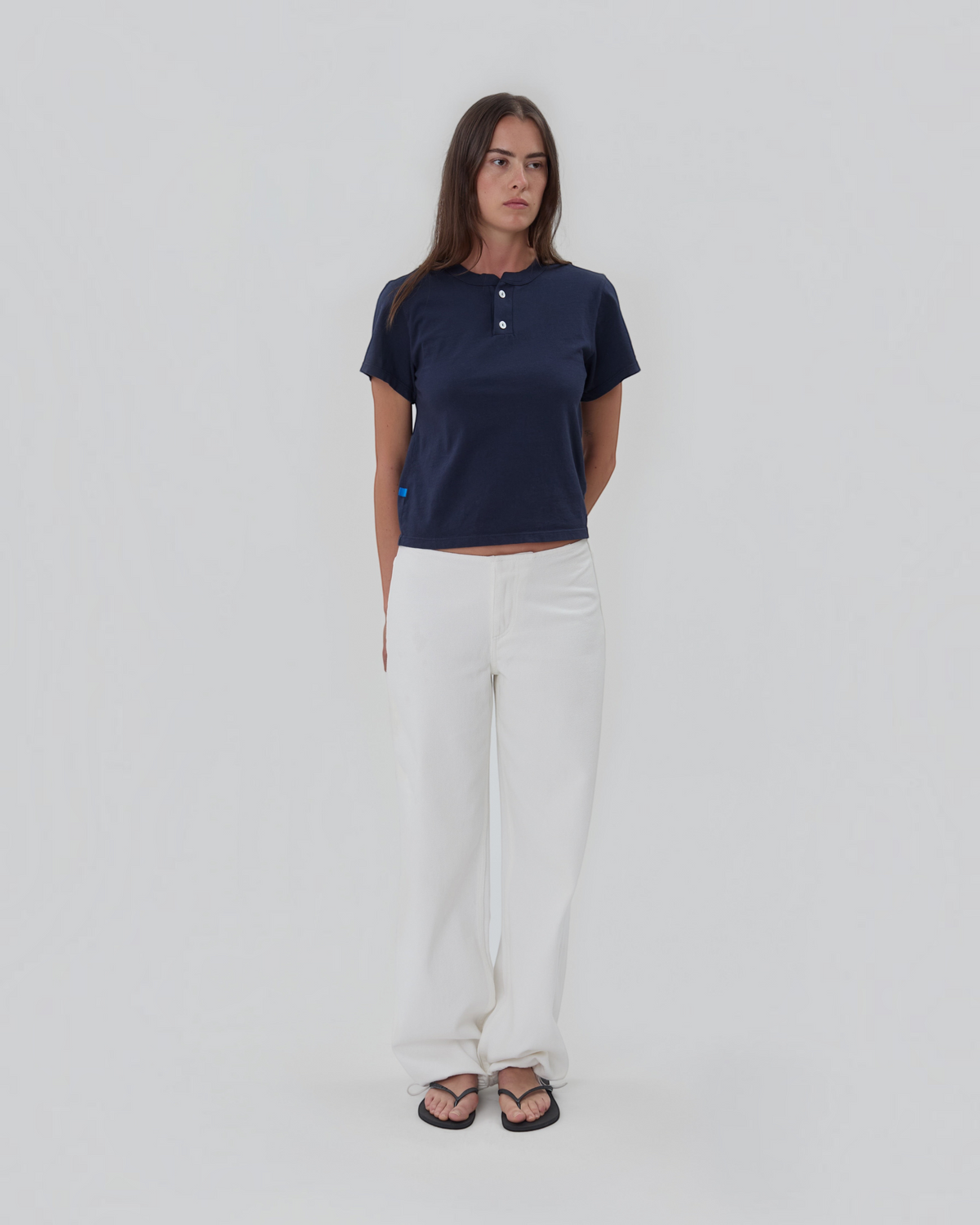 Weldun model wearing a navy blue short sleeve Henley shirt in 100% cotton with a two-button placket and white trousers.