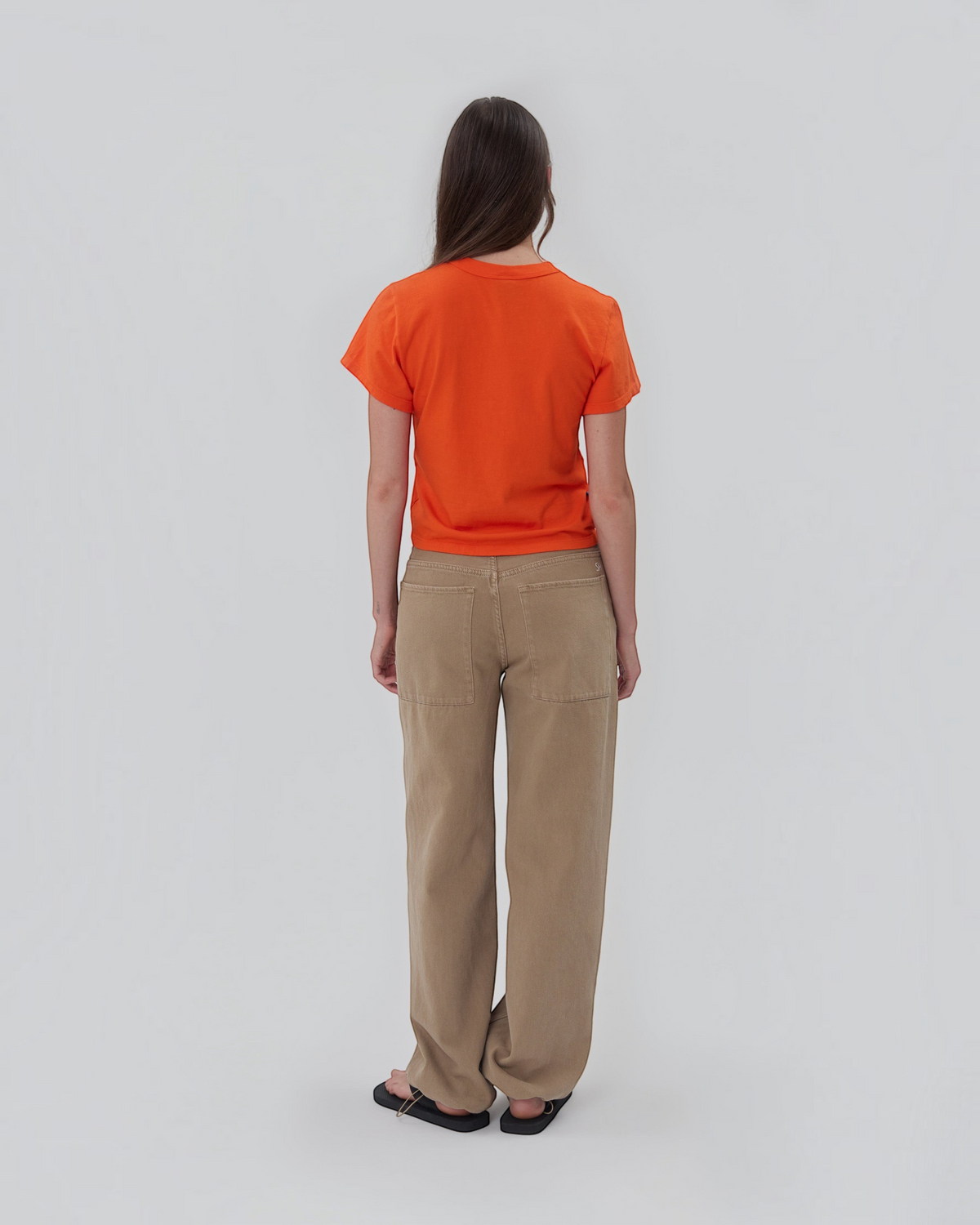 Weldun Still Here orange cotton short sleeve Henley shirt worn by a model from the back view with beige trousers.