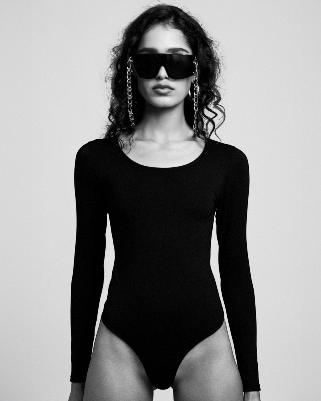 Weldun Donna long-sleeve black scoop neck bodysuit in soft stretch-knit fabric worn by a model with chain sunglasses.