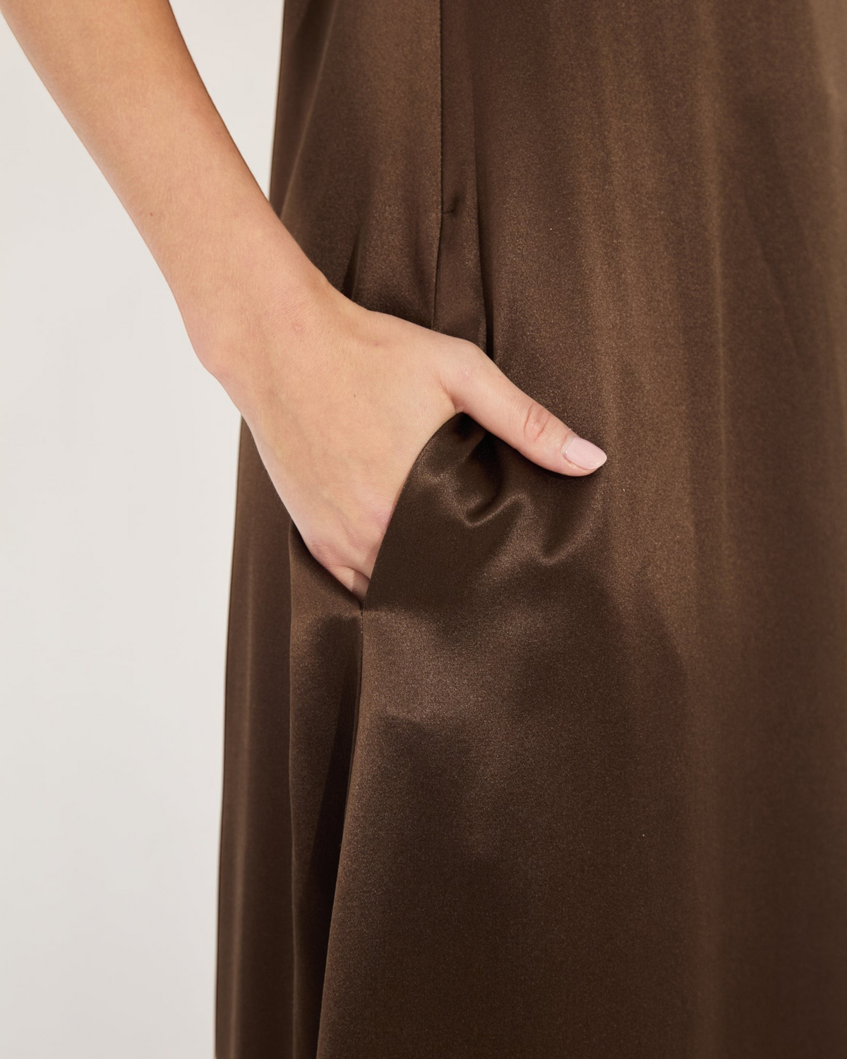 Close-up of a hand in the side pocket of a Weldun Edith Gown, crafted from smooth, chocolate brown silk satin.