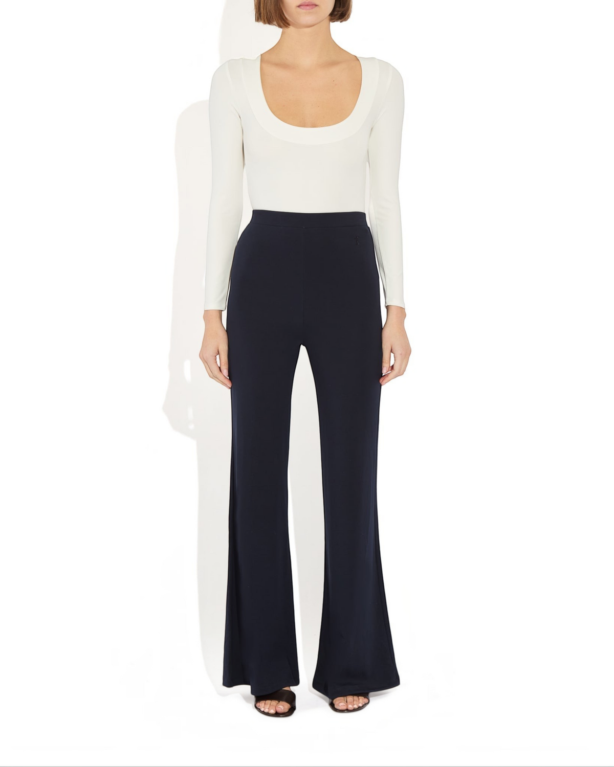 Weldun Maranda Bodysuit in white with a low scoop neckline and long sleeves worn with dark navy flared trousers