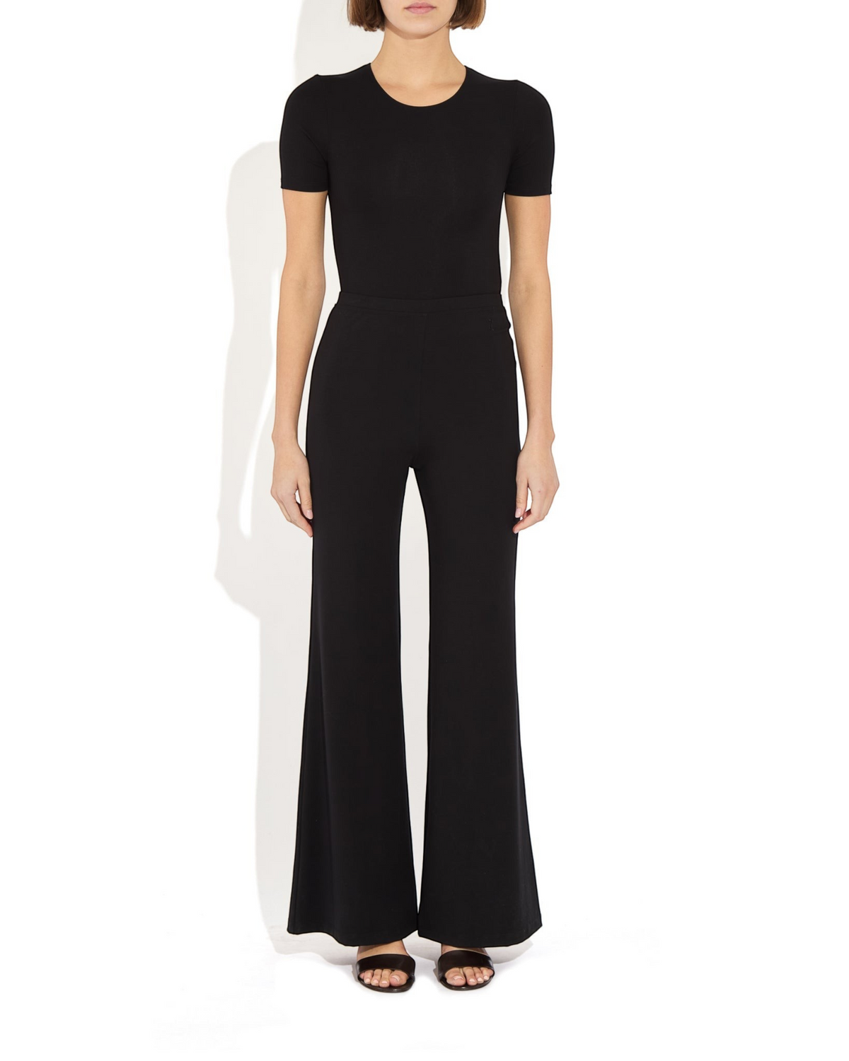 Weldun Penny Bodysuit in black MicroTencel with a ballerina neckline and short sleeves worn with wide-leg trousers.