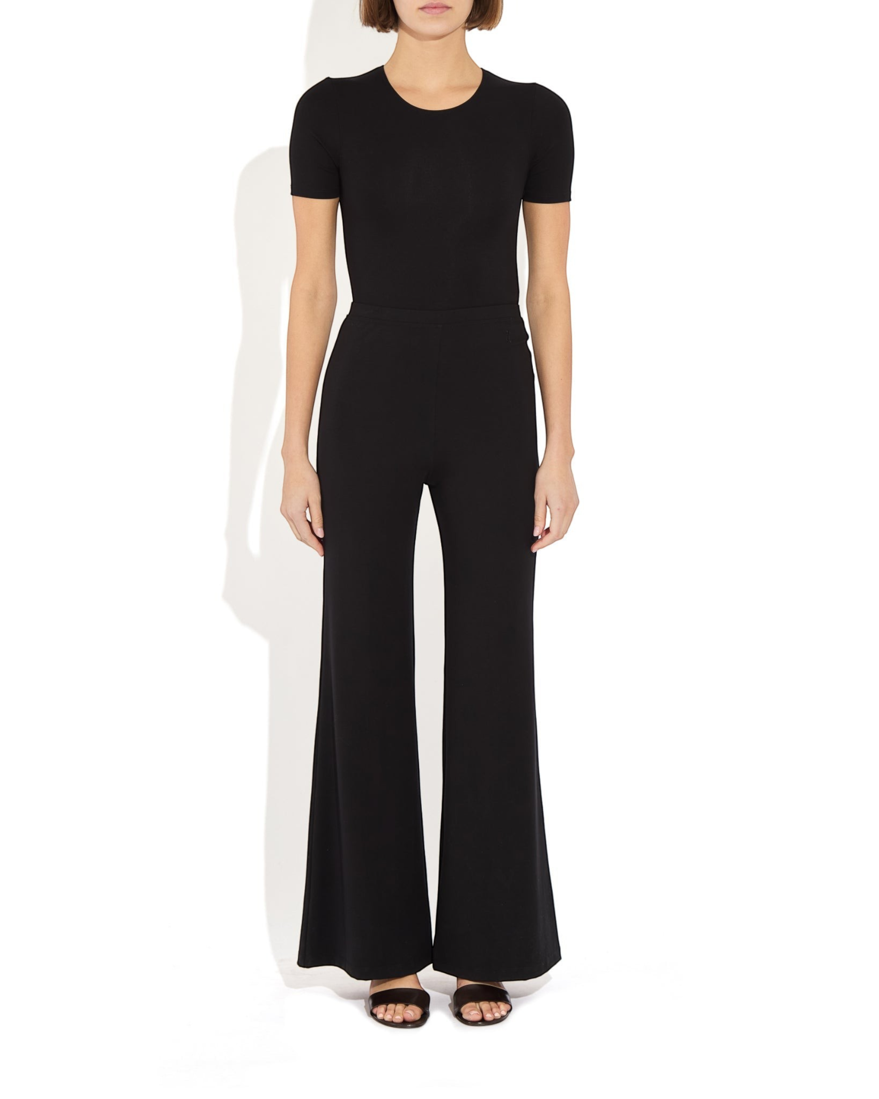 Weldun Penny Bodysuit in black MicroTencel with a ballerina neckline and short sleeves worn with wide-leg trousers.