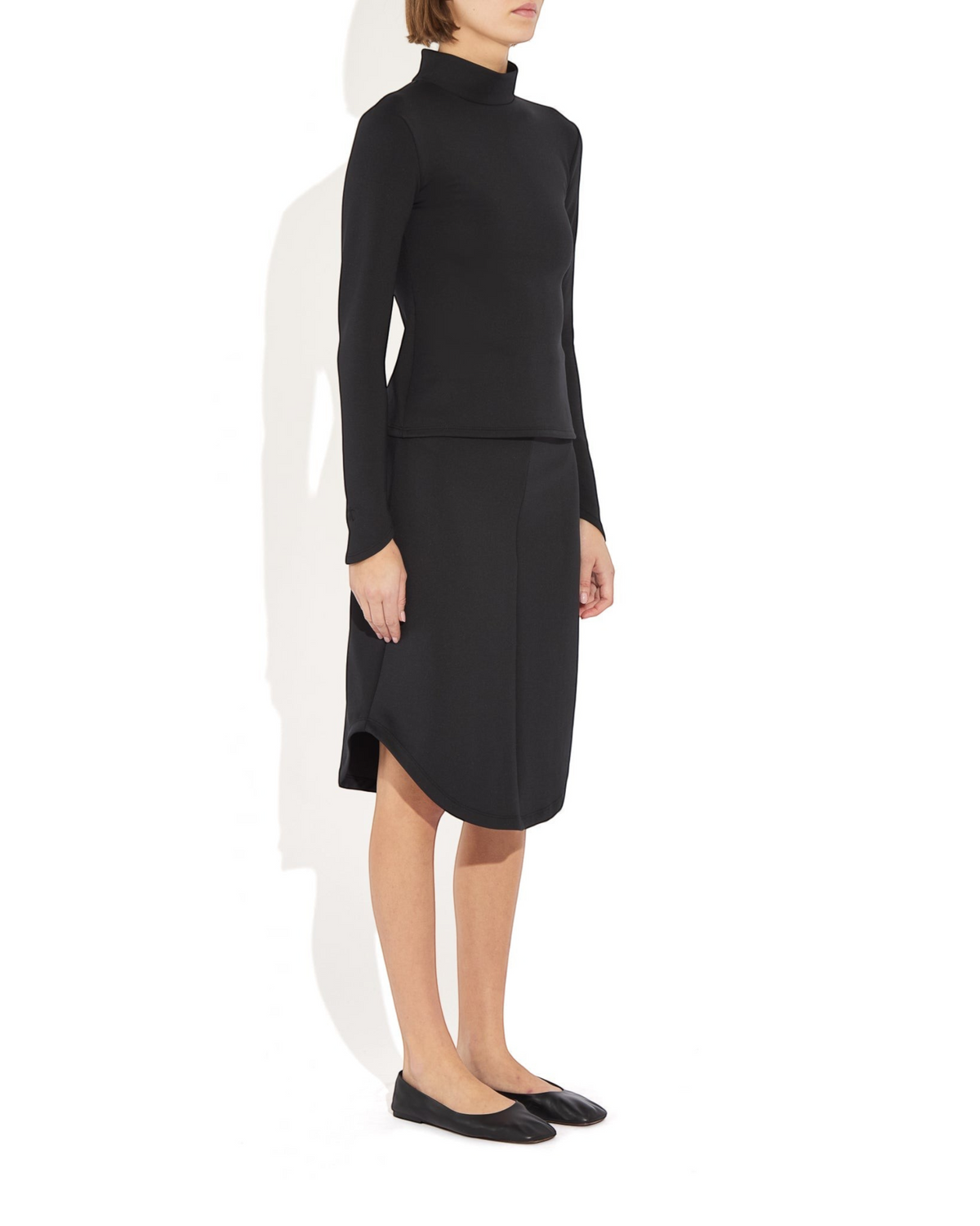 Weldun Rose Skirt in black stretch recycled-poly blend with a sculptural rounded hem, worn by a model in profile.