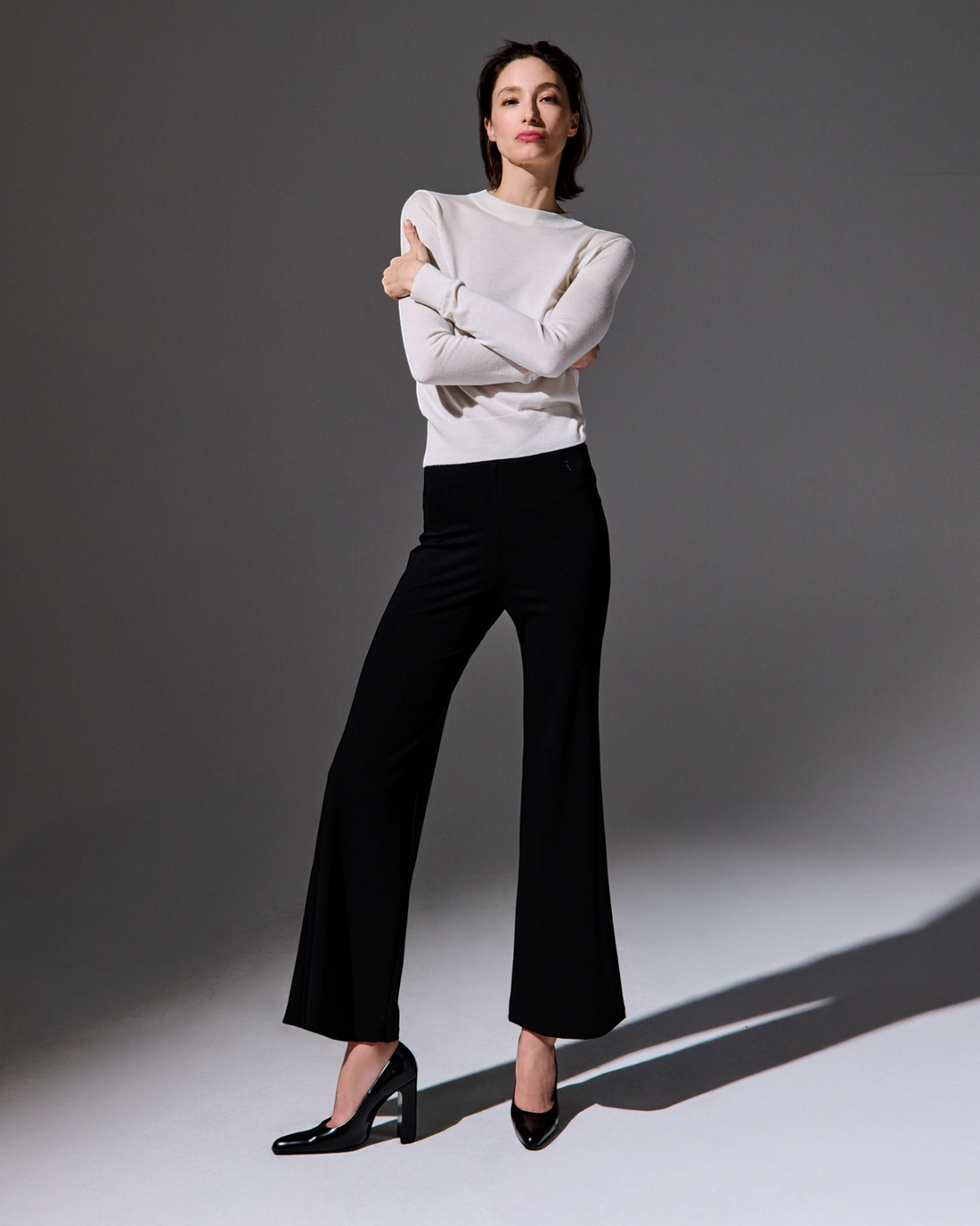 Model wearing Weldun Tessa long black flared pants with a high elastic waist and a white long-sleeve top