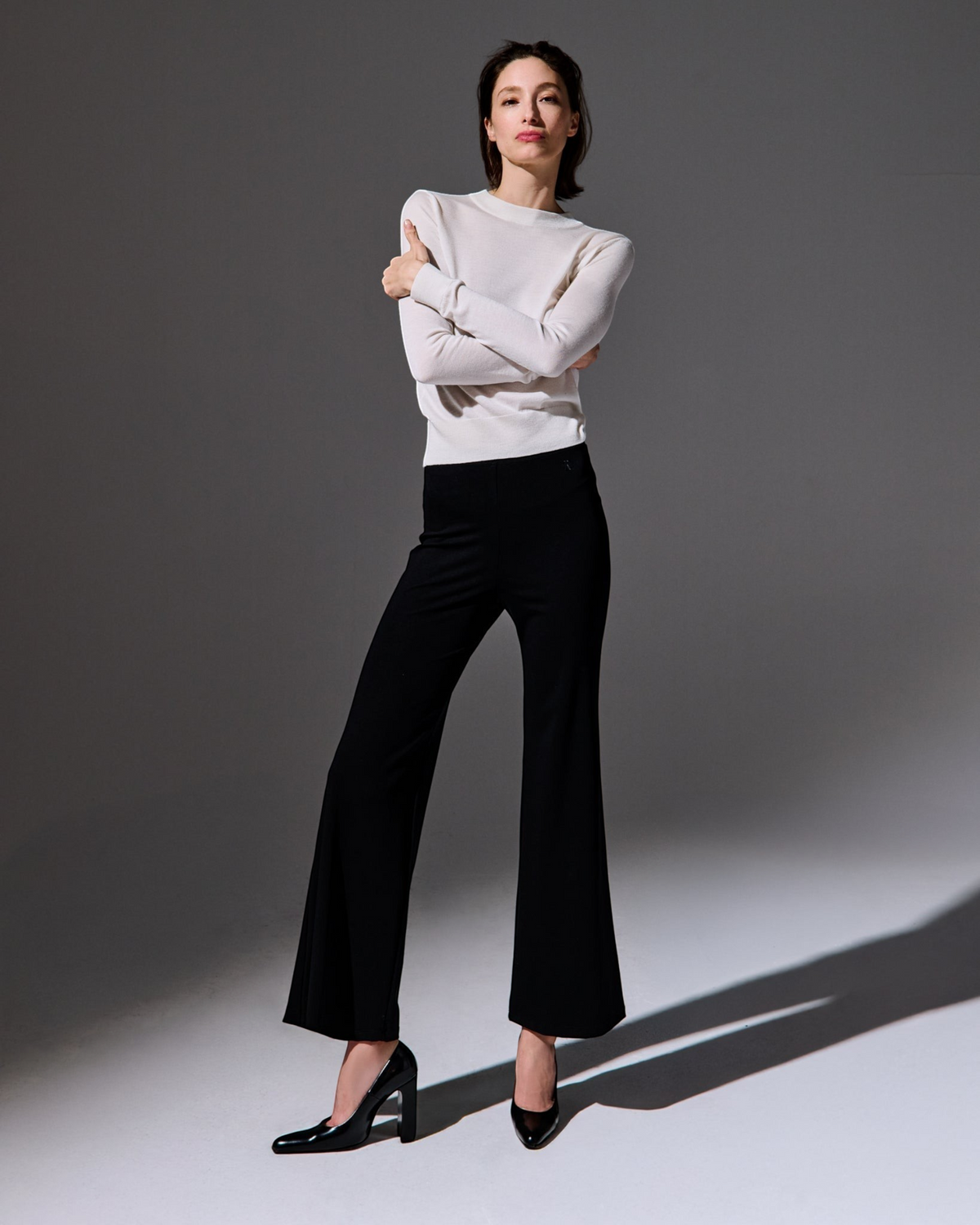 Model wearing Weldun Tessa long black flared pants with a high elastic waist and a white long-sleeve top
