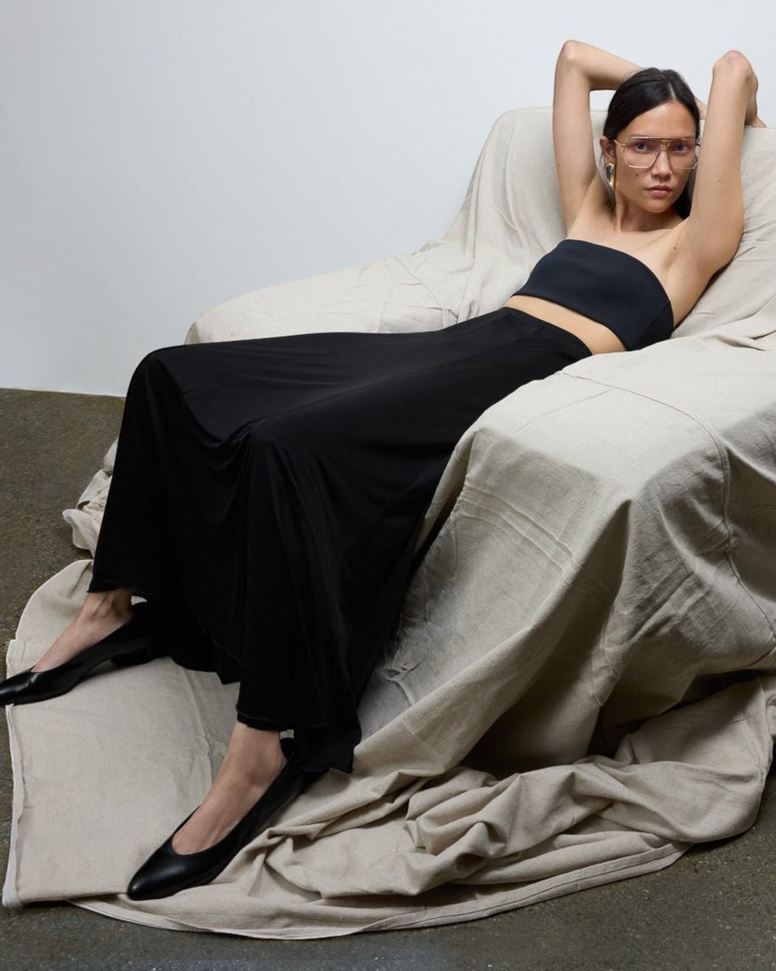 Model wearing a Weldun black semi-sheer Olivia maxi skirt in soft lyocell fabric while lounging in a chair.