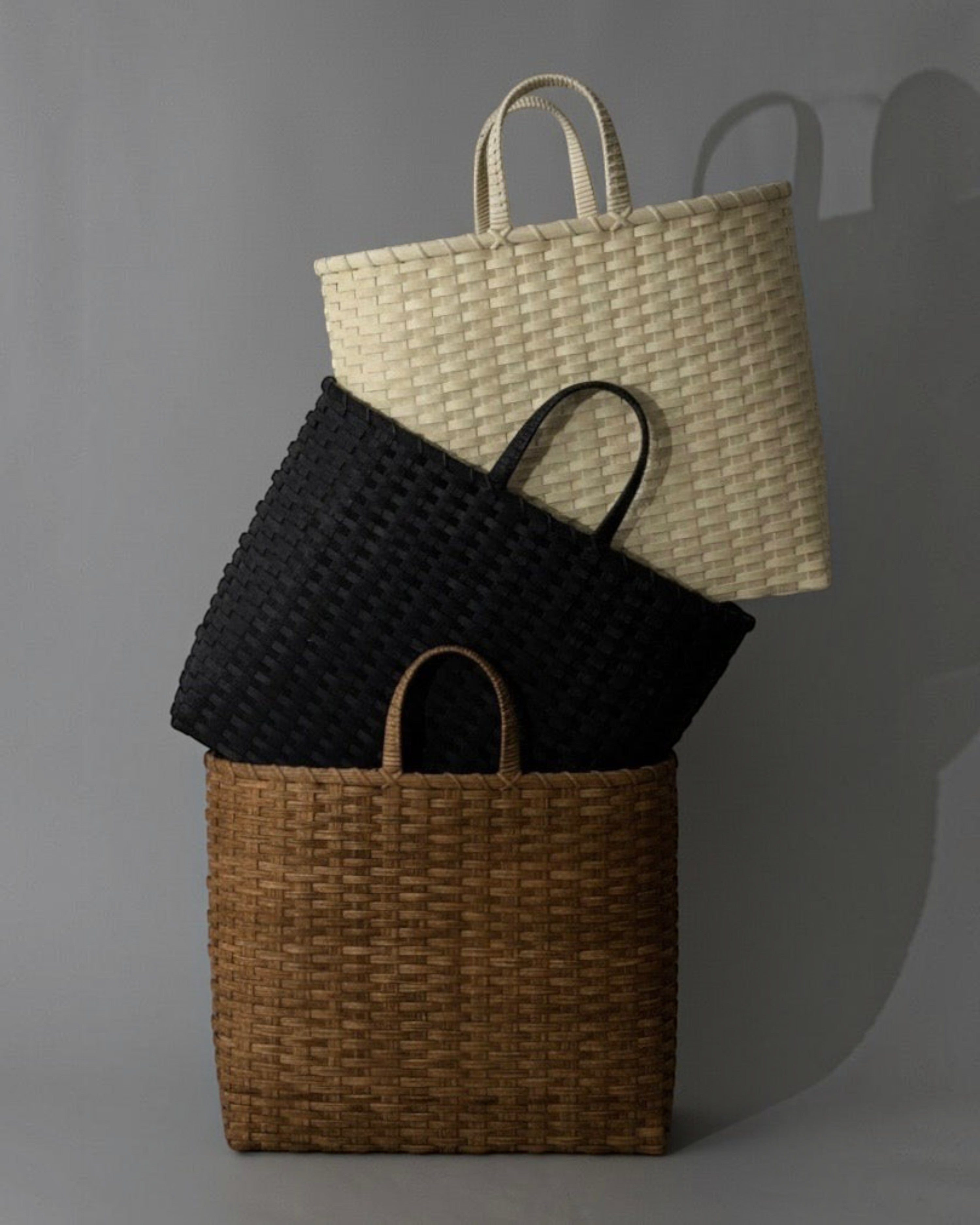 Weldun Big Shopper oversized rattan baskets in cream, black, and brown stacked against a grey background.