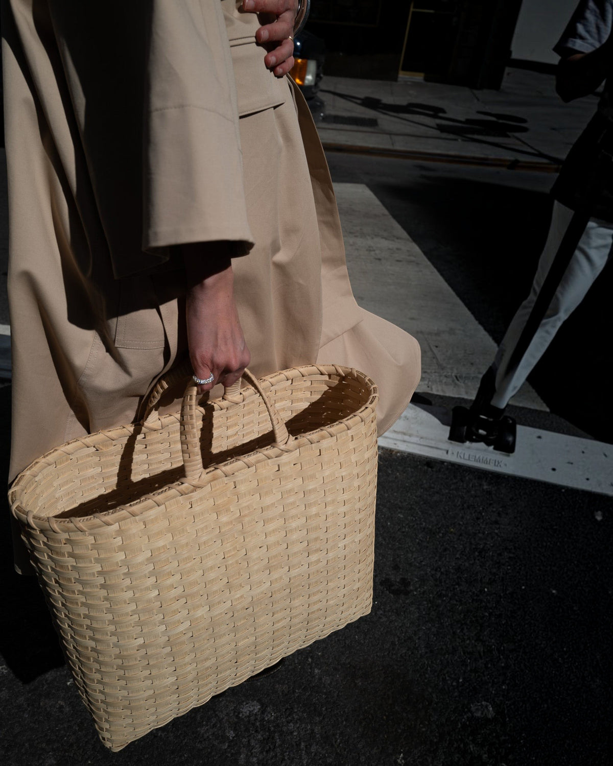 Weldun oversized rattan Big Shopper basket in natural beige held by a person wearing a tan trench coat on a city street