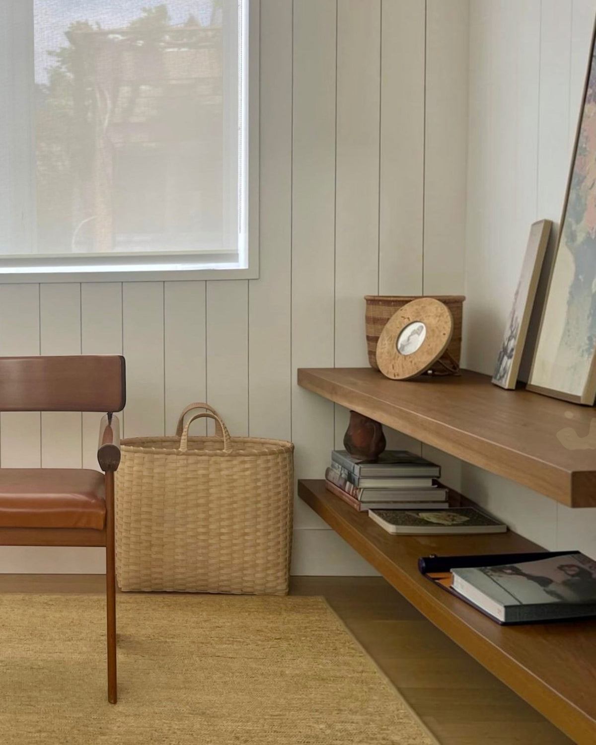 Weldun Big Shopper oversized rattan basket sitting on a floor next to a leather chair in a minimalist living room.