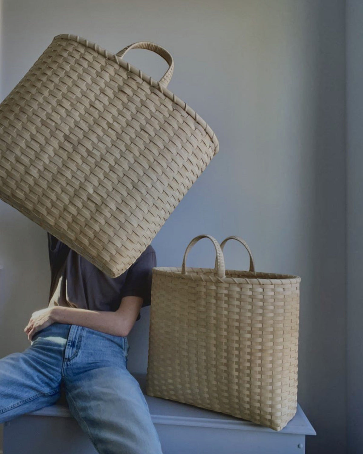 Weldun Big Shopper oversized rattan basket with woven texture, held by a person wearing jeans and a grey t-shirt.