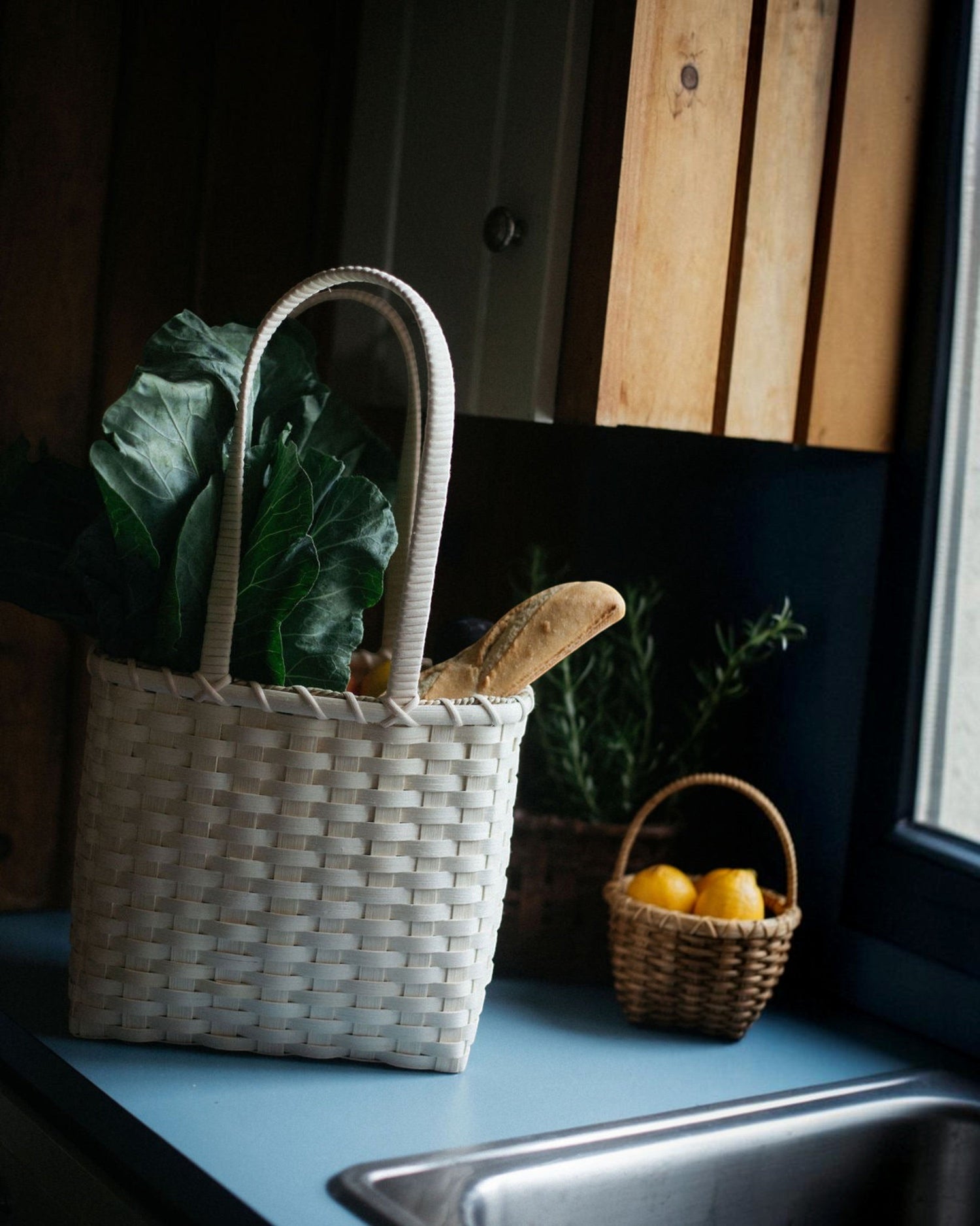 Weldun Carol lunch basket hand-woven from natural rattan with a shoulder strap, filled with greens and bread.