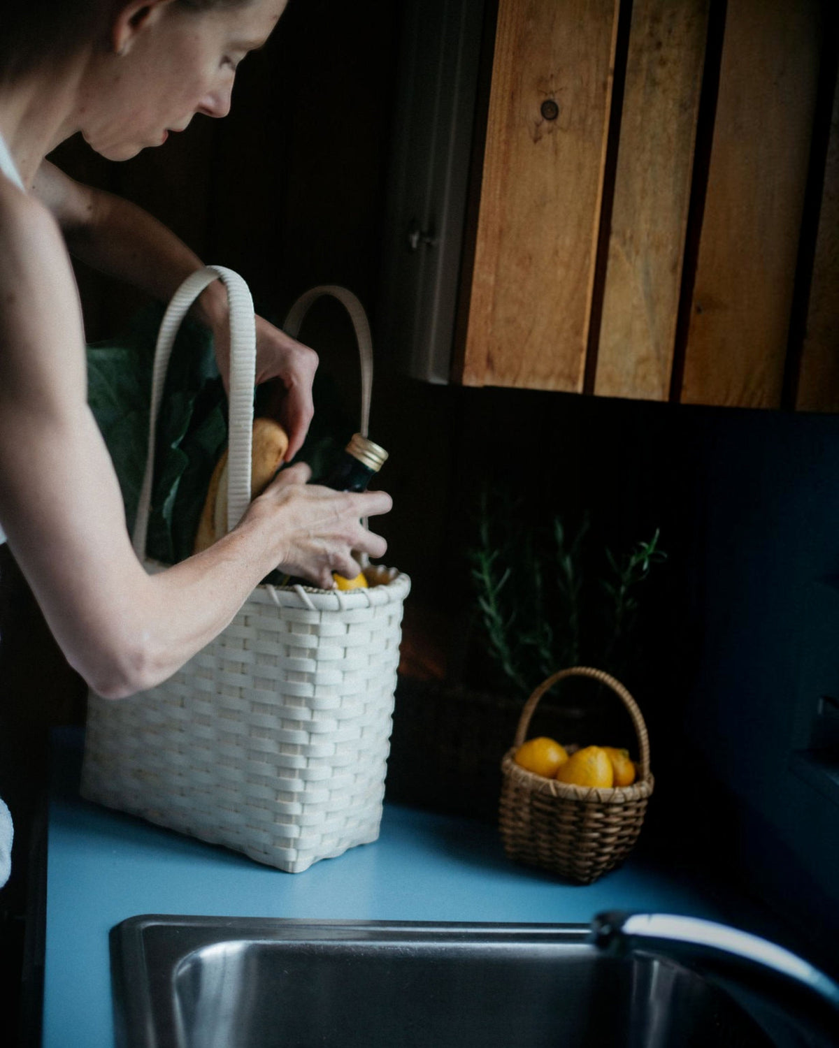 Weldun Carol Lunch Basket hand-woven from natural rattan with a shoulder strap, held by a person in a kitchen.