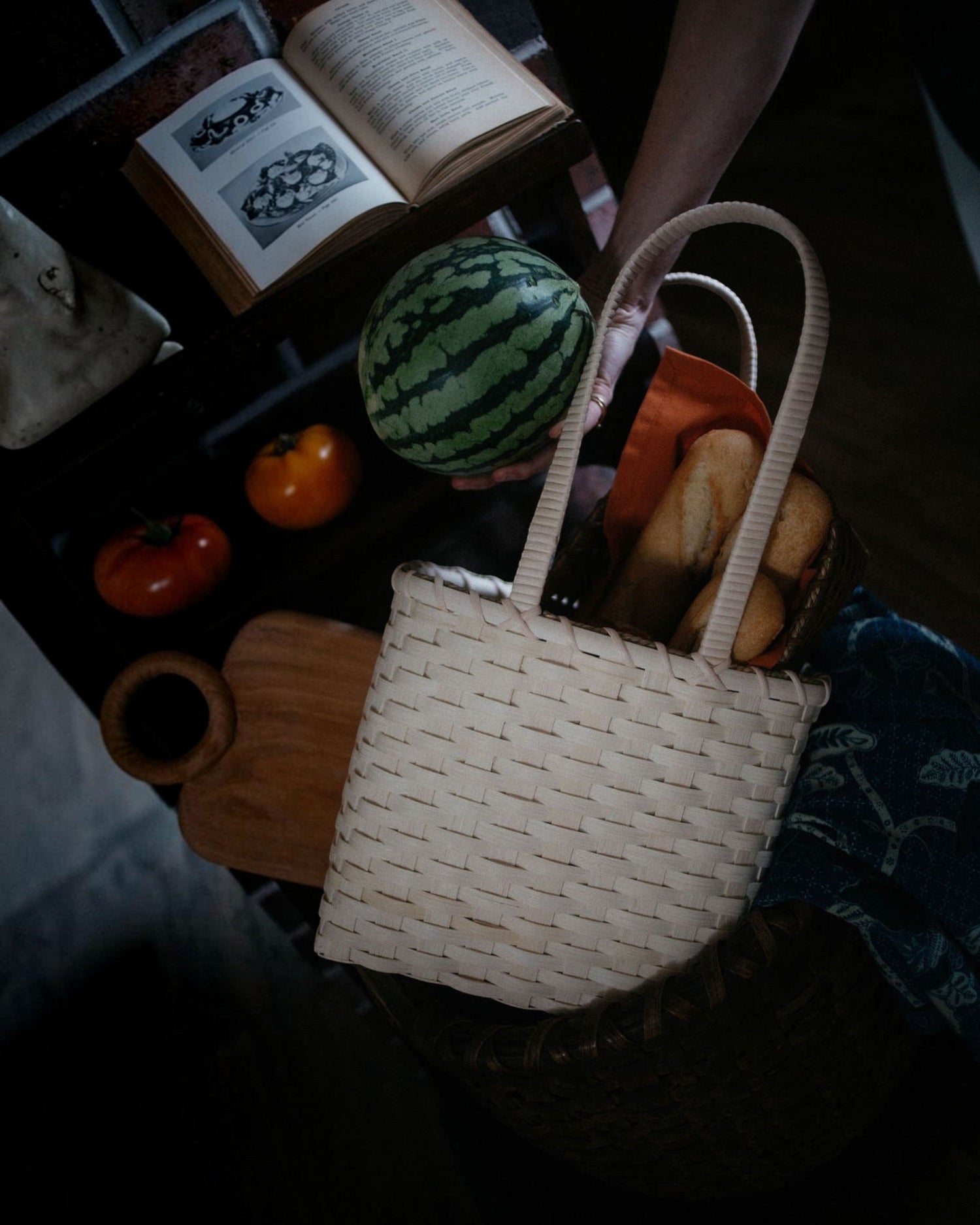 Weldun Carol Lunch Basket hand-woven from natural rattan with a long shoulder strap, holding bread and fruit.